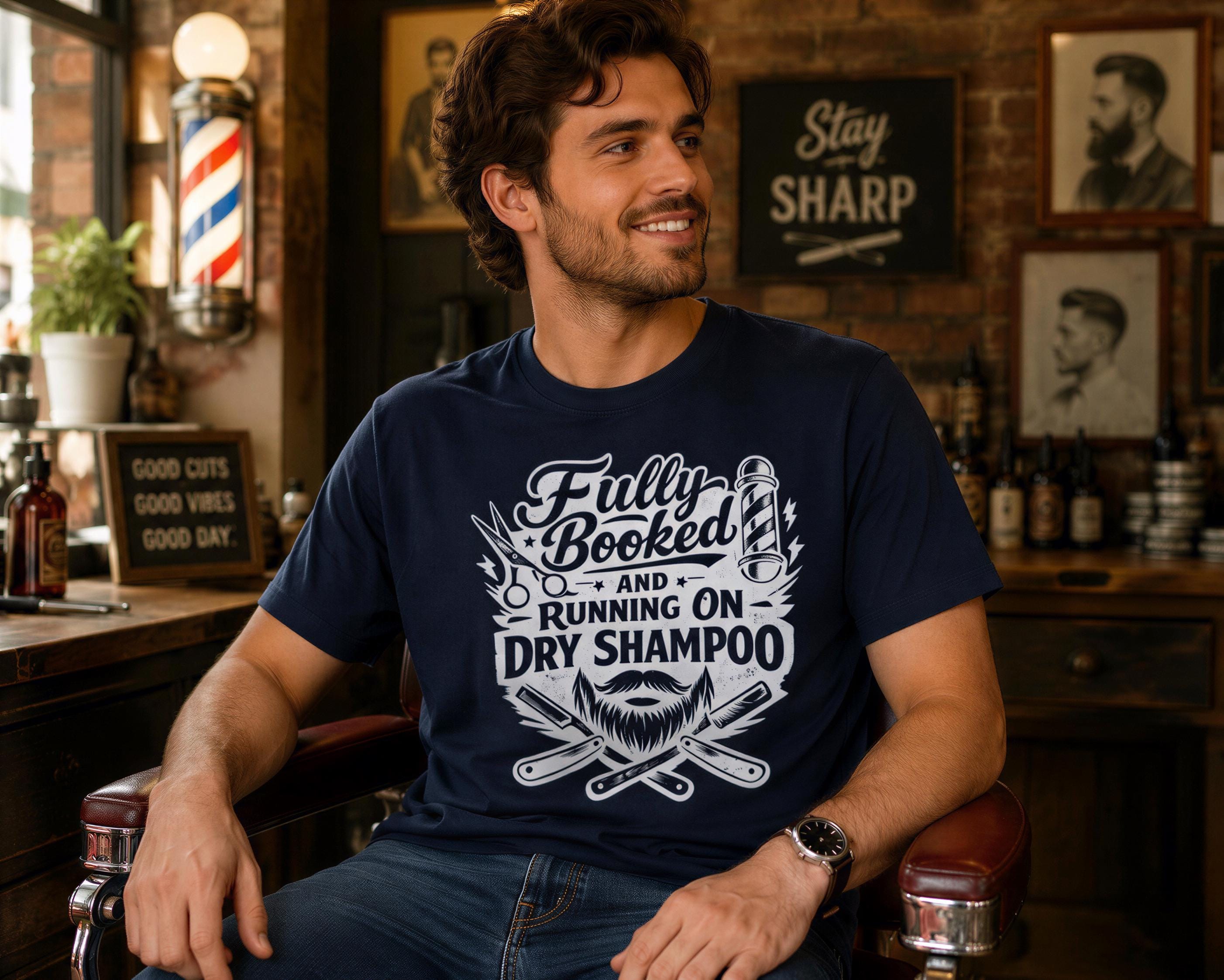 A man wearing a navy blue t-shirt with a graphic design is sitting in a barber shop, smiling and looking to the side.