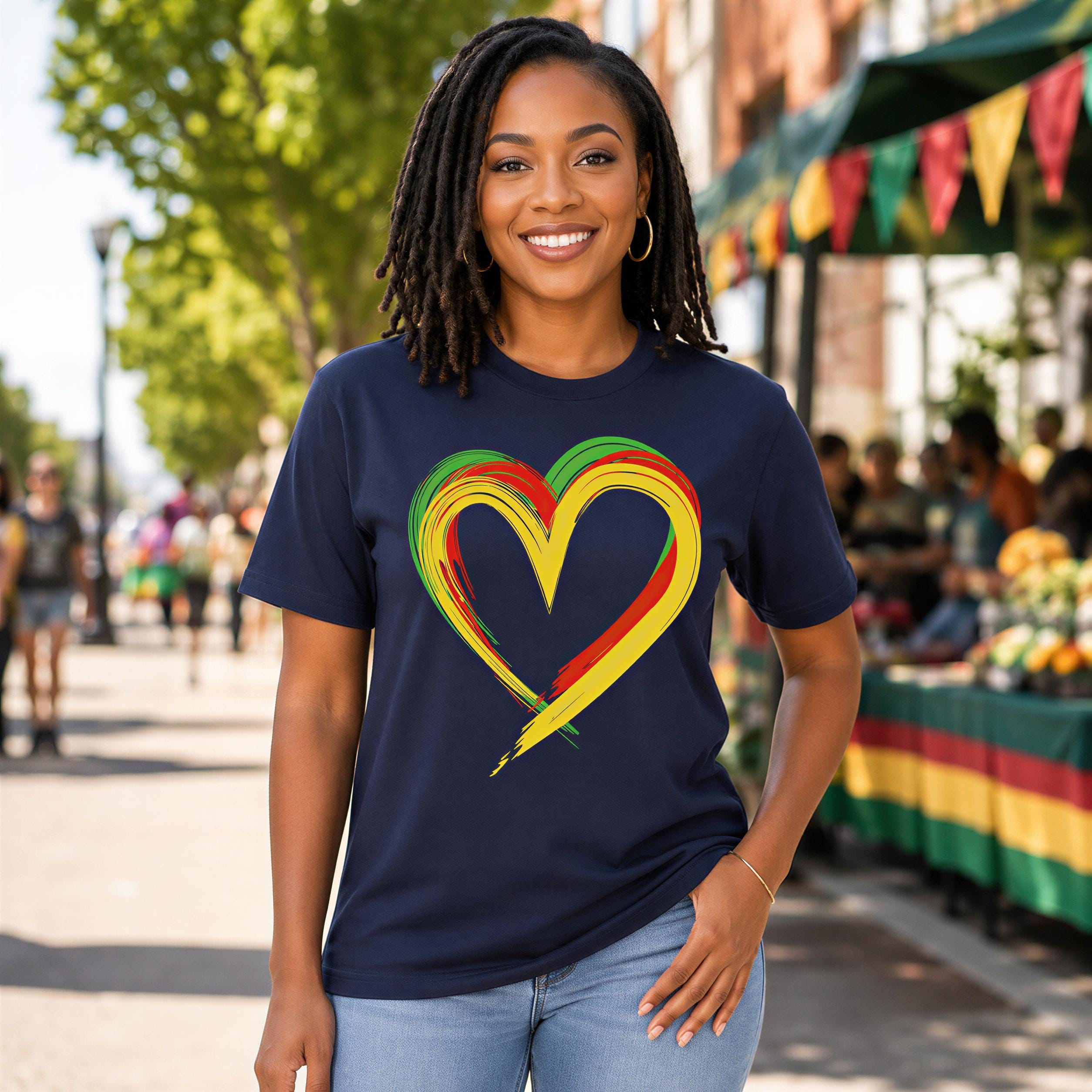 A smiling woman wearing a navy blue t-shirt with a colorful heart design stands in front of a crowd at an outdoor event.
