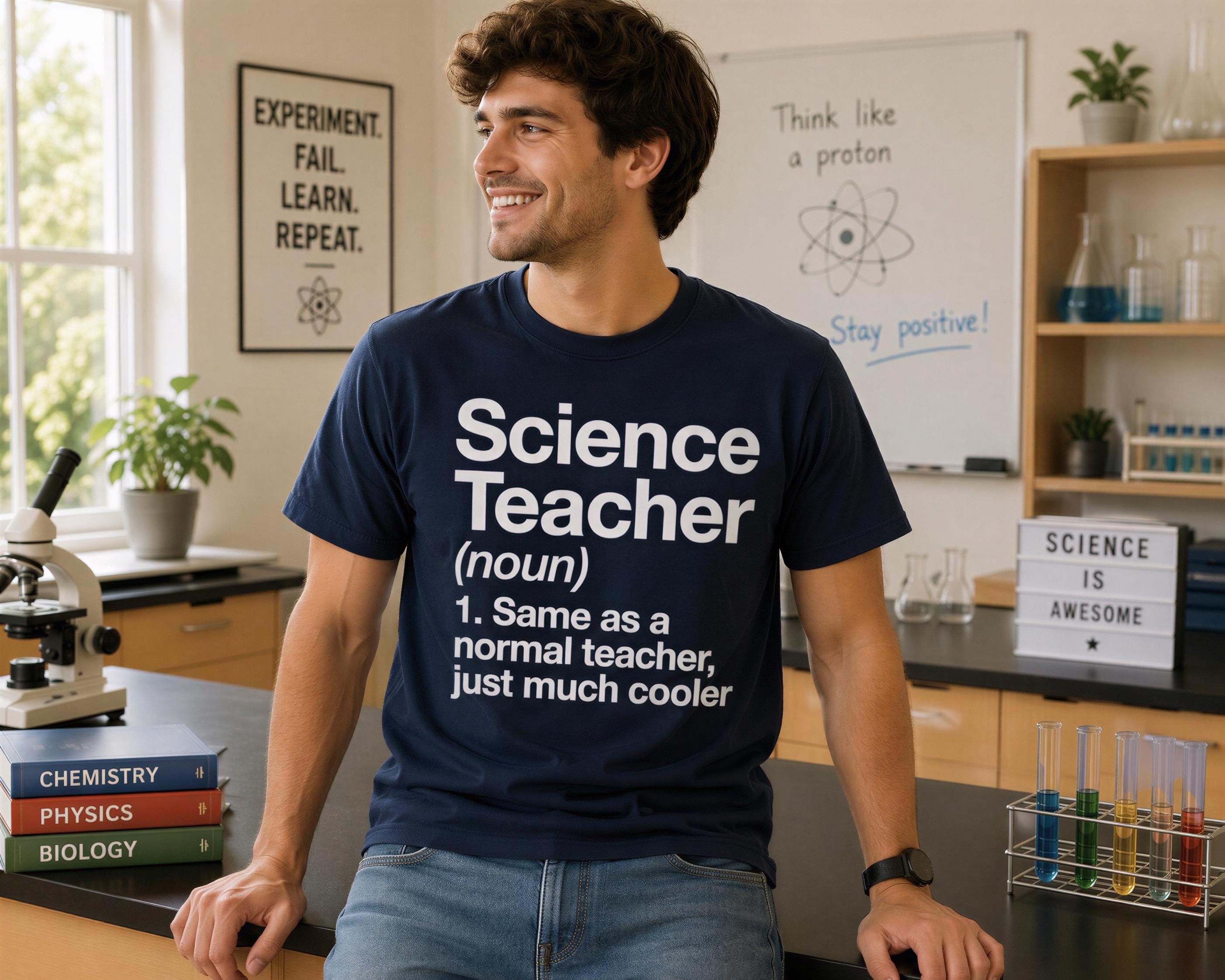 A man wearing a blue t-shirt with the definition of a science teacher, smiling and standing in a laboratory setting with various scientific equipment and books visible.