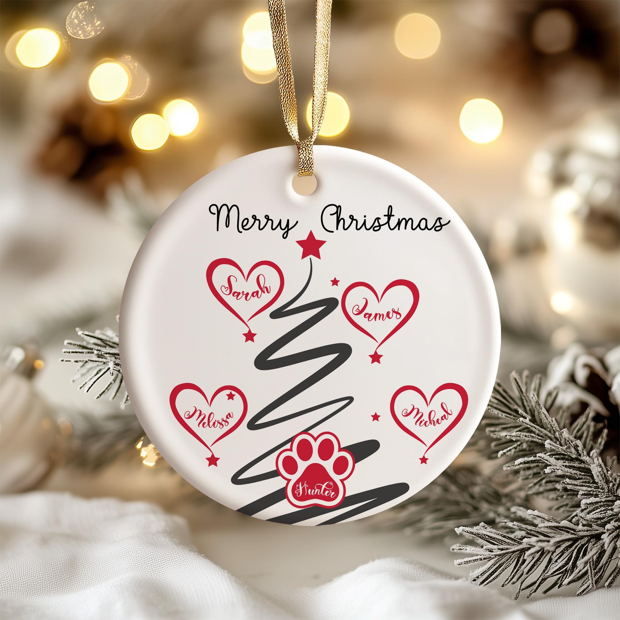 A white Christmas ornament with a black and red design, featuring a tree with red hearts and a paw print, and the text "Merry Christmas" and names of people.