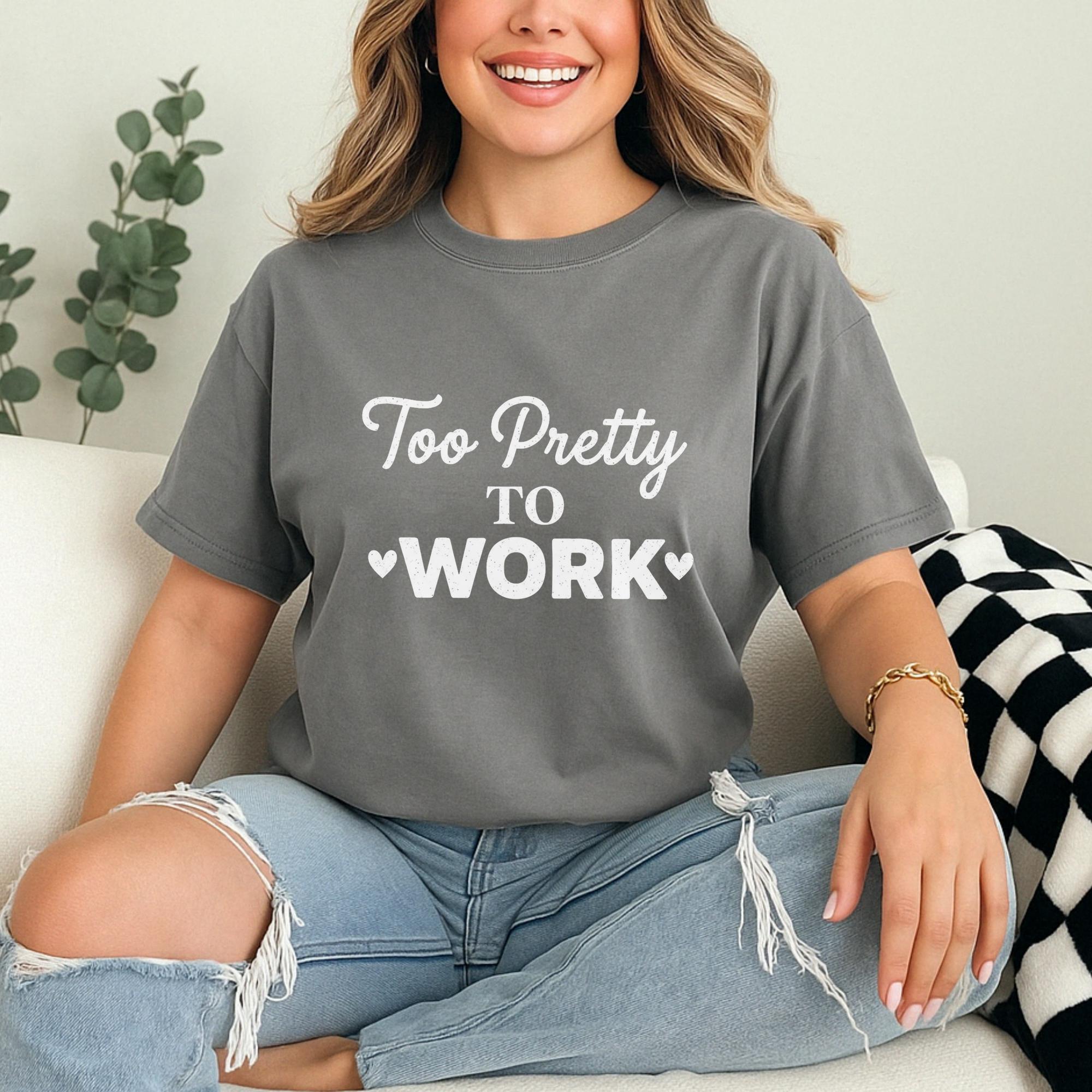 A woman wearing a gray t-shirt with the text "Too Pretty to Work" is sitting on a couch, smiling.