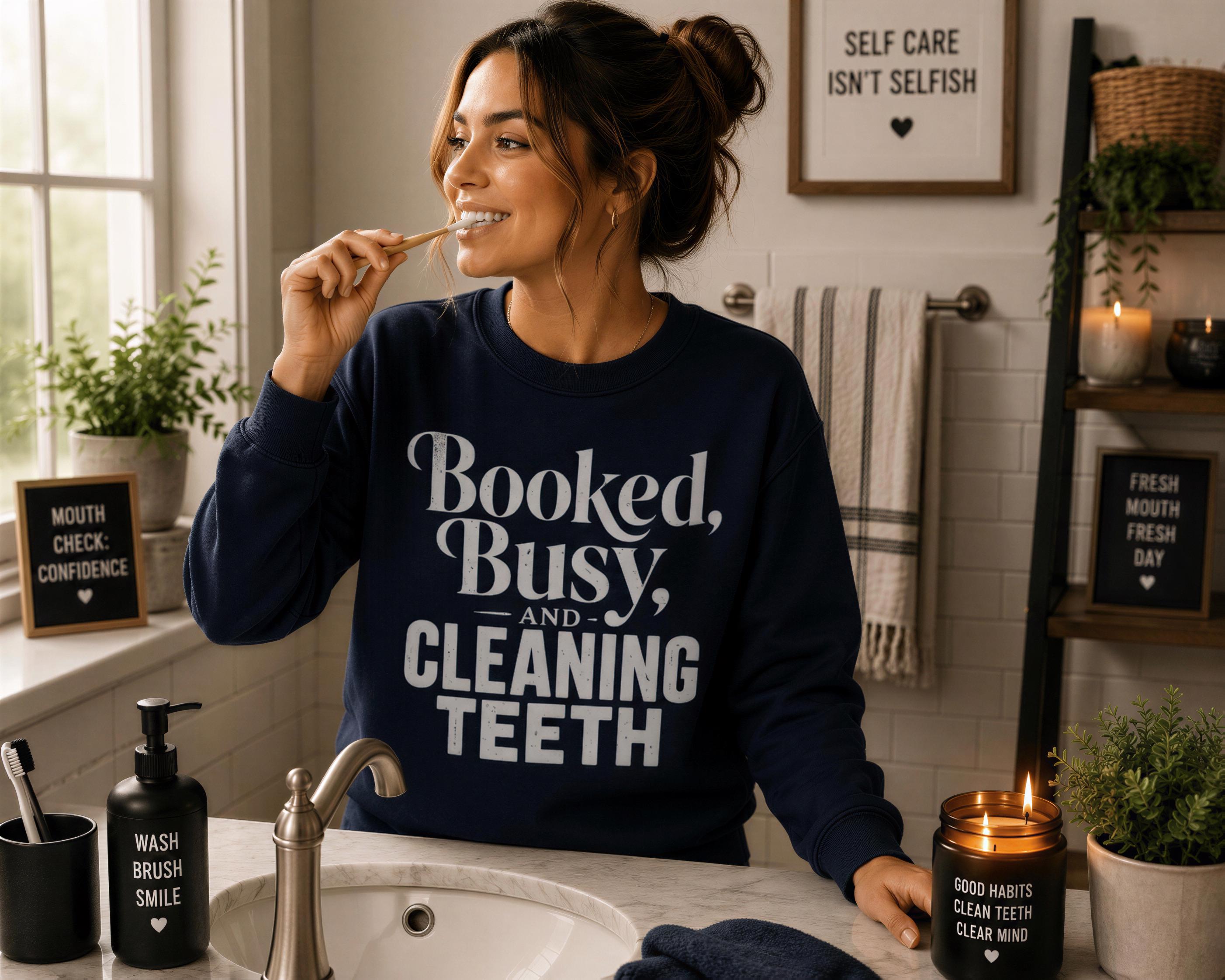 A woman in a navy blue sweatshirt brushing her teeth in a bathroom with a sink, toothbrush, and candles.