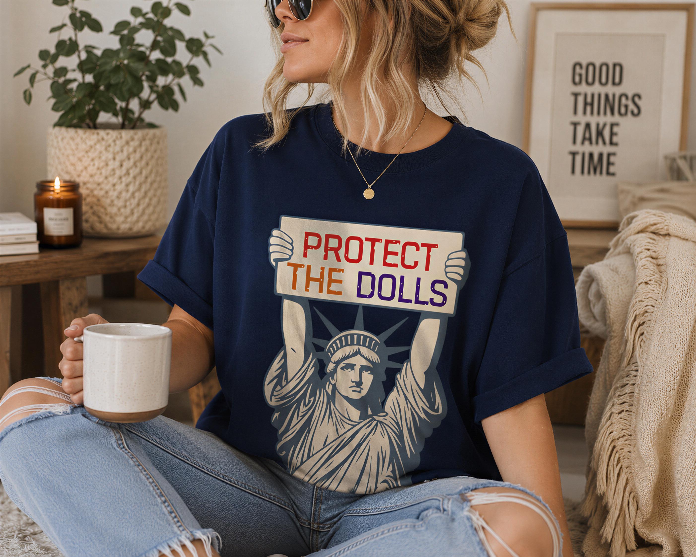 A woman wearing a blue t-shirt with a graphic design and holding a coffee mug is sitting in a room with a potted plant and a framed quote on the wall.