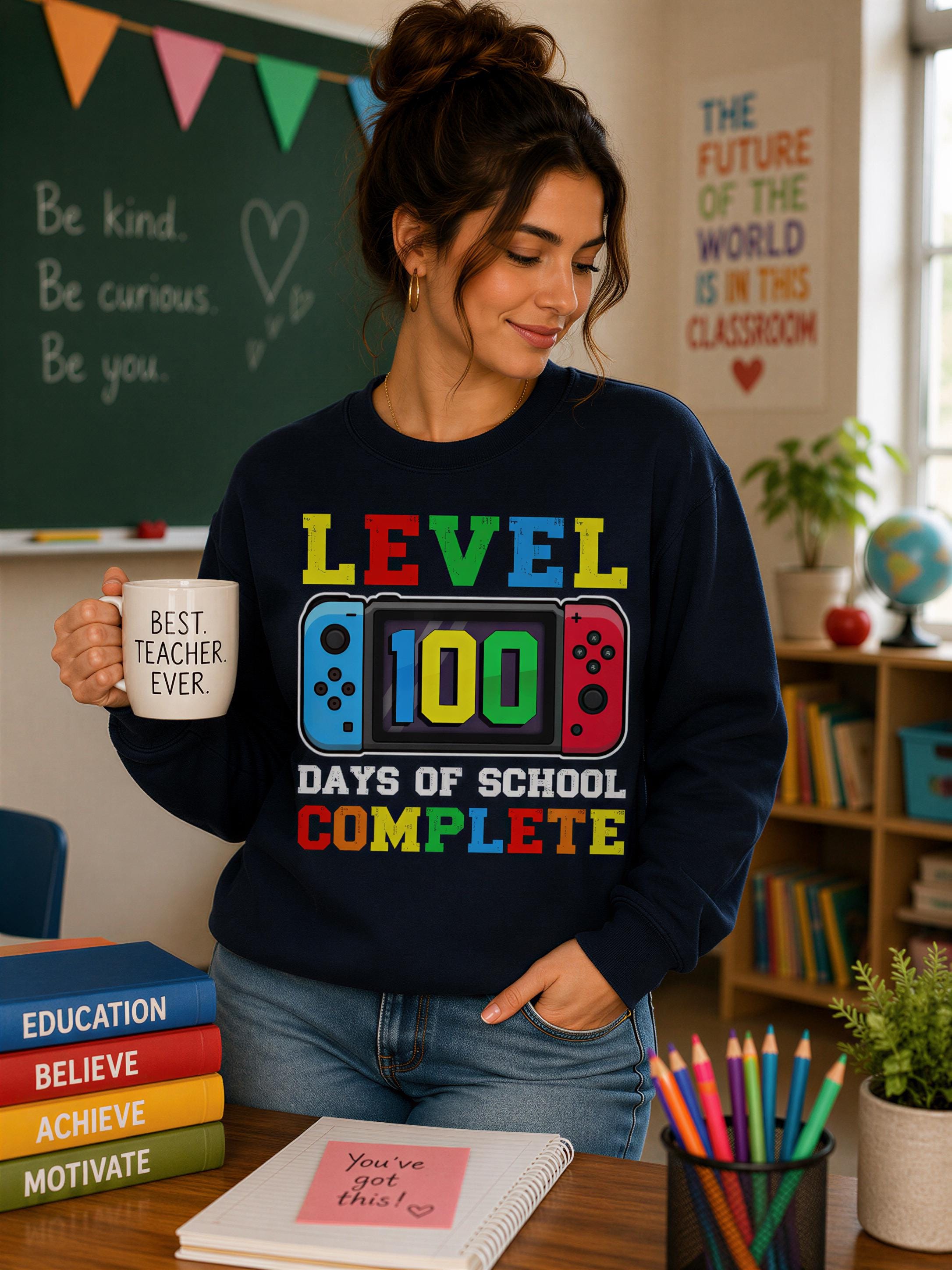 A woman wearing a black sweatshirt with a colorful graphic stands in a classroom, holding a mug and surrounded by books and a plant.