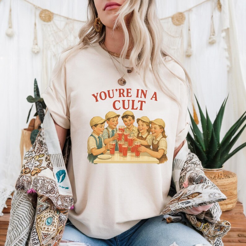 A woman wearing a white t-shirt with a graphic design of a group of people enjoying drinks at a table.