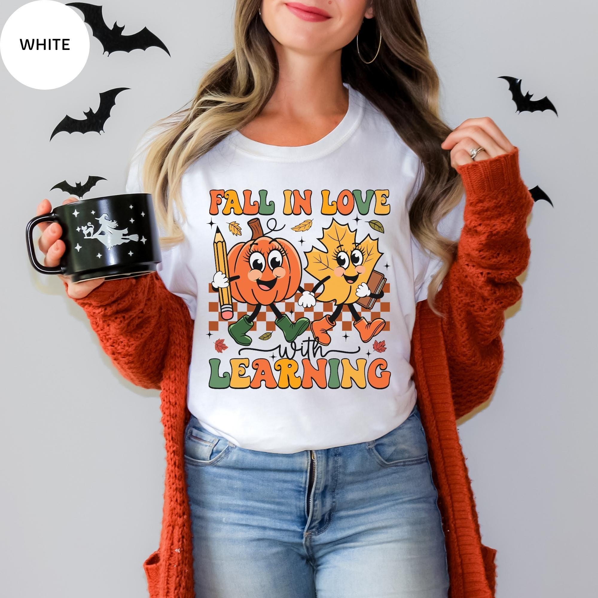 A woman wearing a white t-shirt with a graphic design of a pumpkin and a leaf, holding a black mug with a pumpkin and leaf design.
