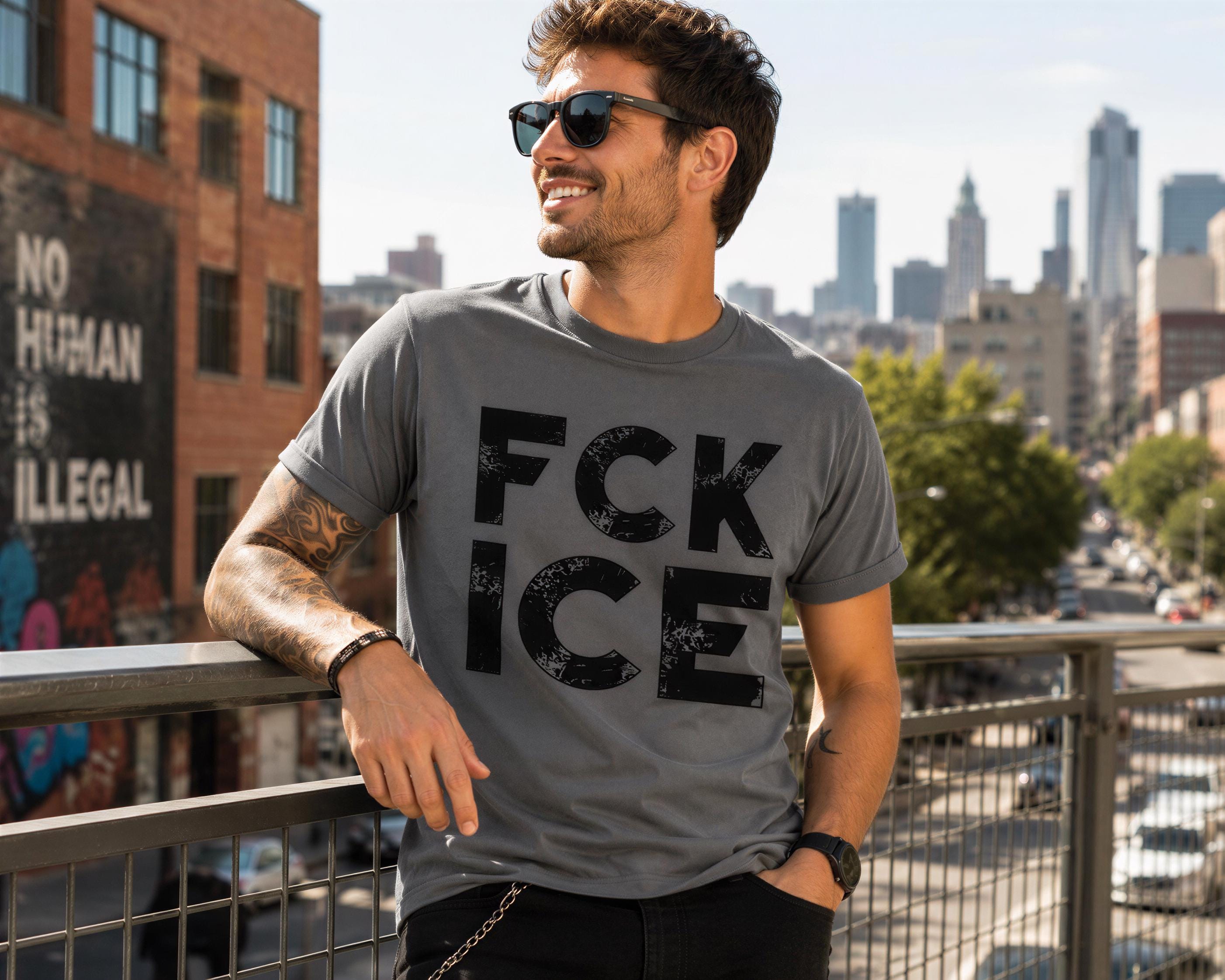 A man wearing a gray t-shirt with the text "Fck Ice" is standing on a bridge overlooking a city skyline.