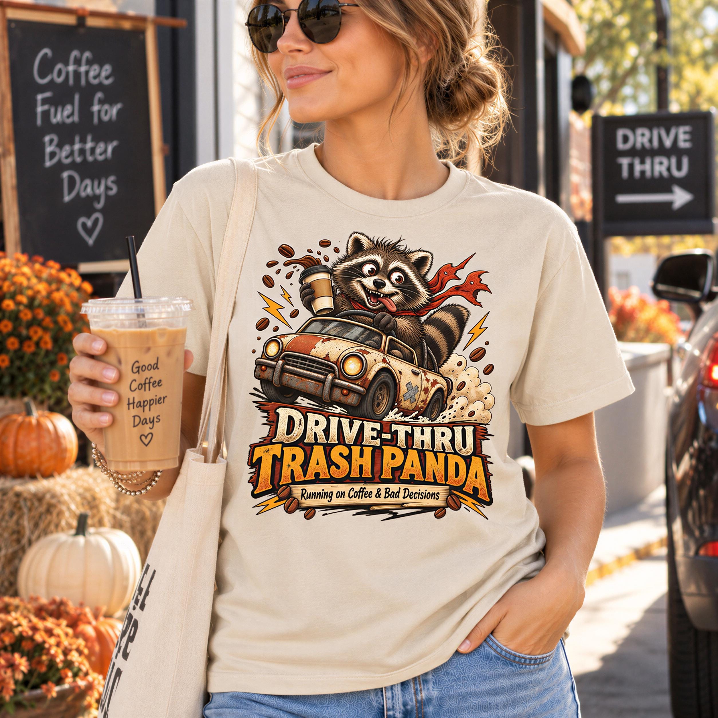 A woman wearing a t-shirt with a raccoon graphic and text, holding a drink and standing in front of a chalkboard sign.