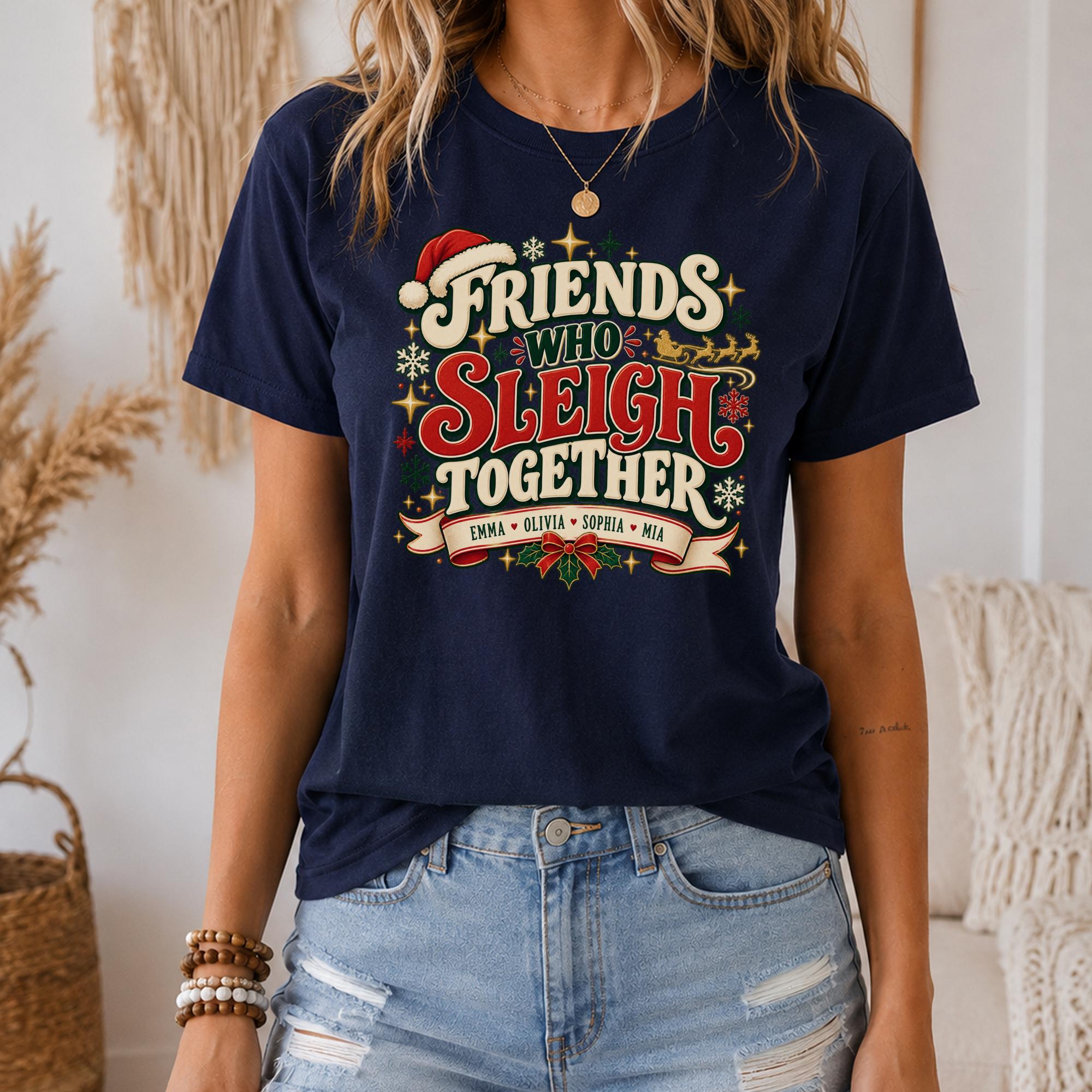 A woman wearing a navy blue t-shirt with a festive design that says "Friends Who Sleigh Together" and includes the text "Emma + Santa + Maria" along with a Santa Claus illustration.