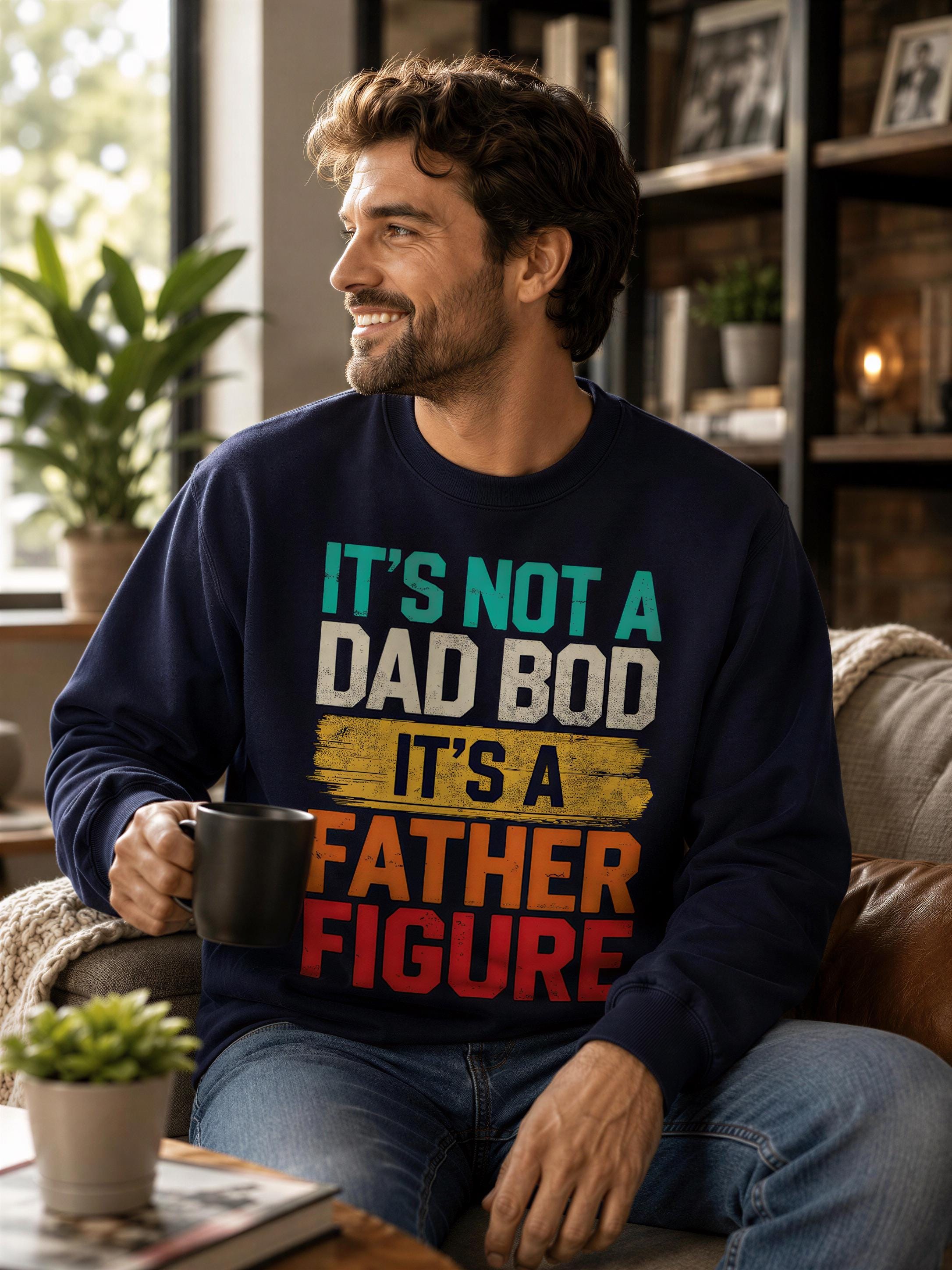A man wearing a blue sweatshirt with text on it is sitting on a couch, holding a black mug and smiling.