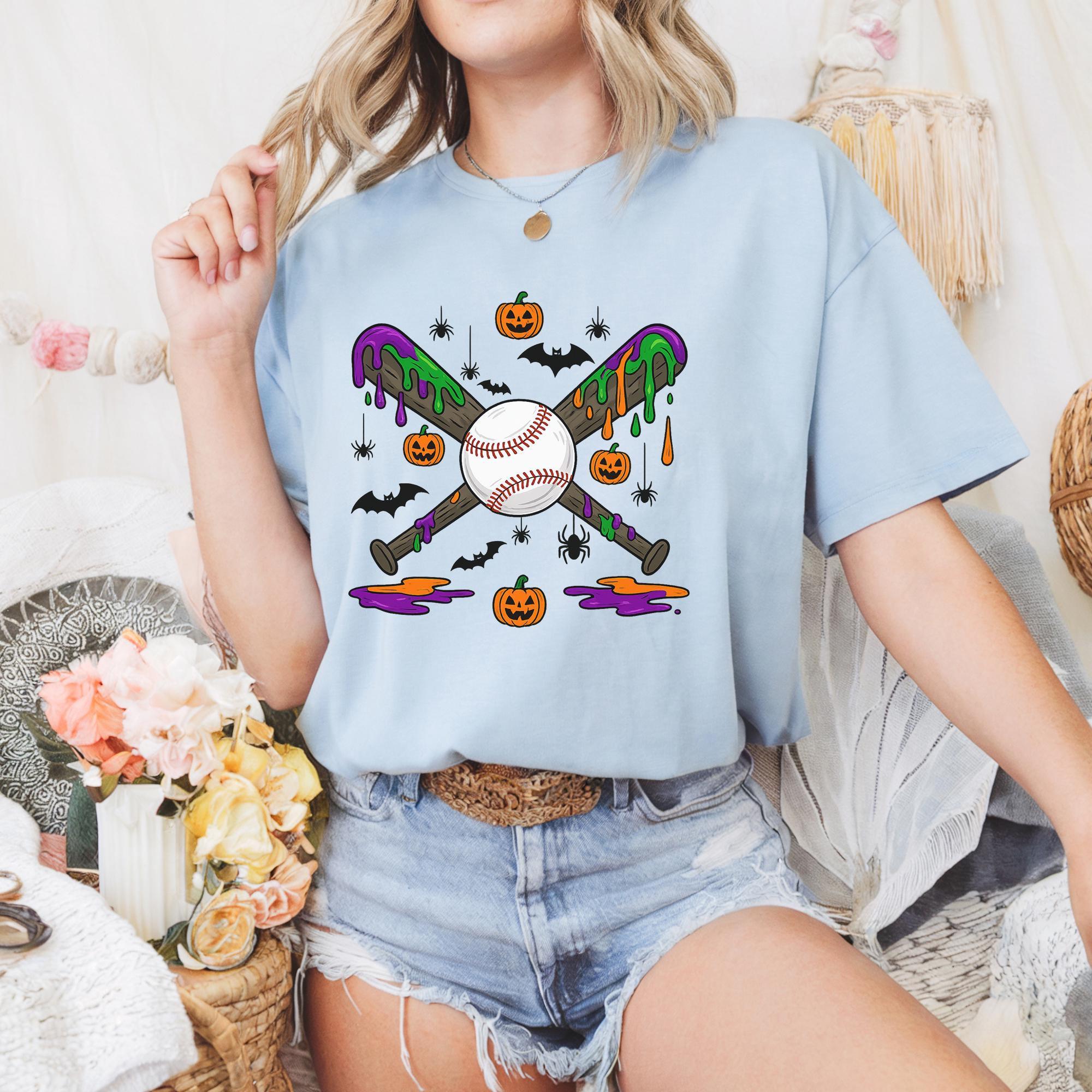 A woman wearing a light blue t-shirt with a graphic design of baseball bats, pumpkins, and bats, along with a necklace and a floral skirt.