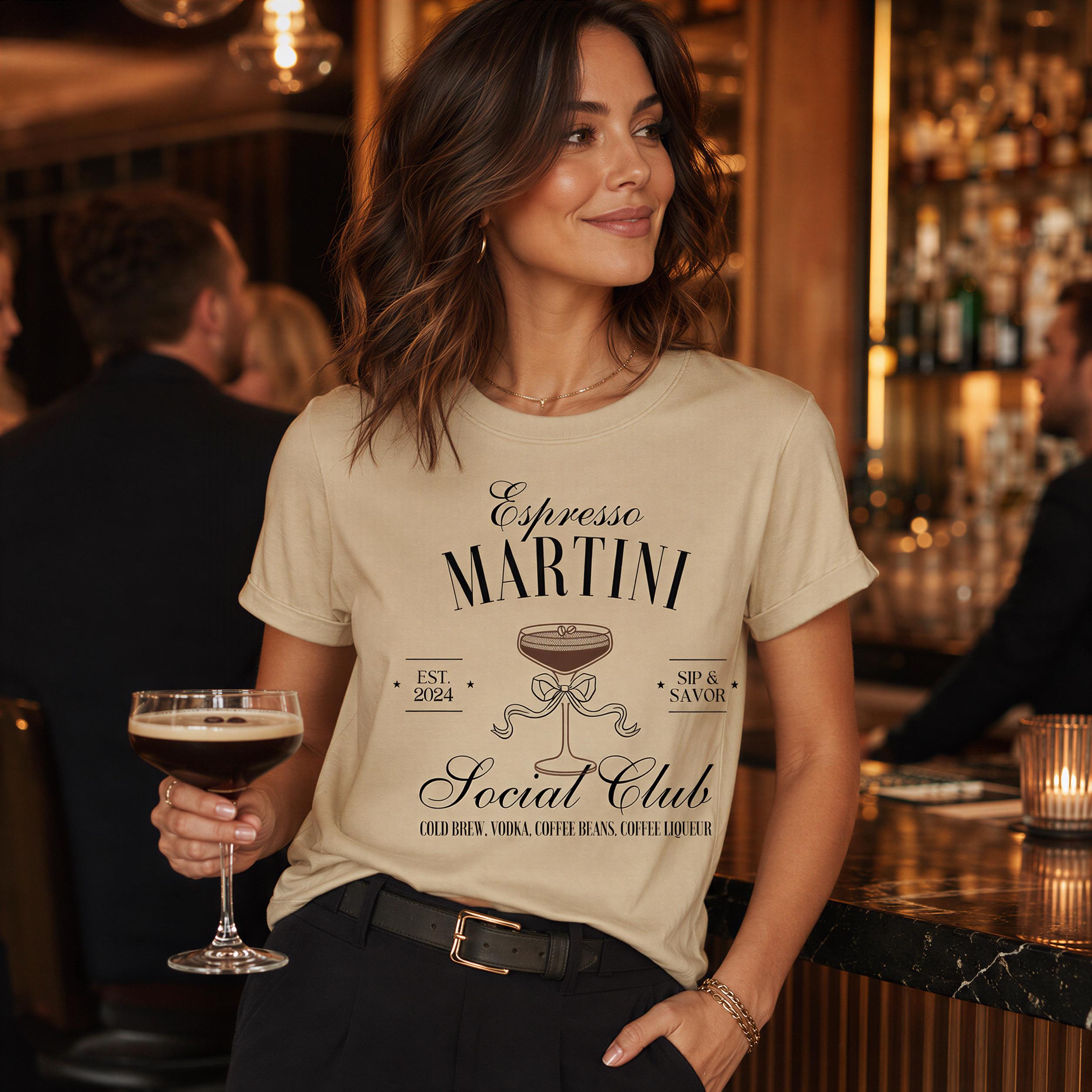 A woman wearing a t-shirt with the text "Espresso Martini Social Club" is holding a glass of espresso martini at a bar.