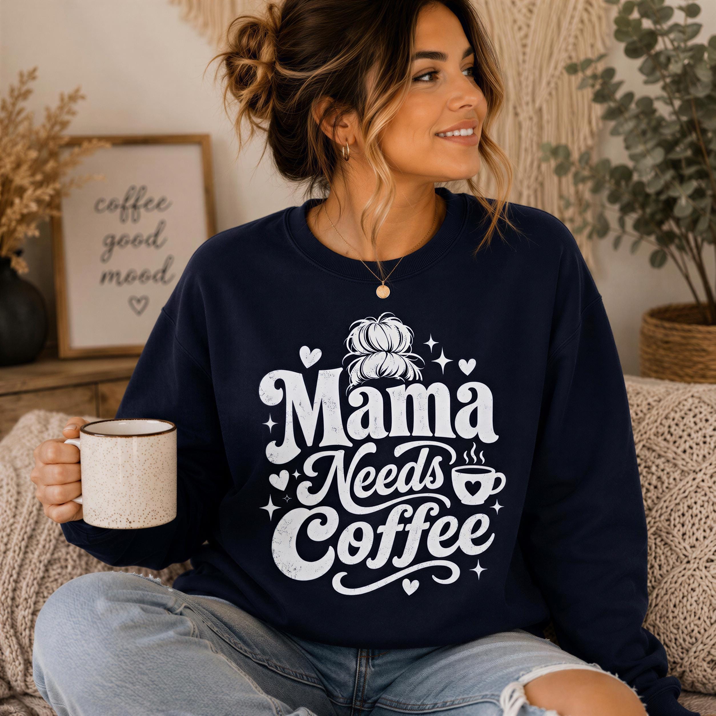 A woman wearing a navy blue sweatshirt with the text "Mama Needs Coffee" is sitting on a couch, holding a coffee mug and smiling.