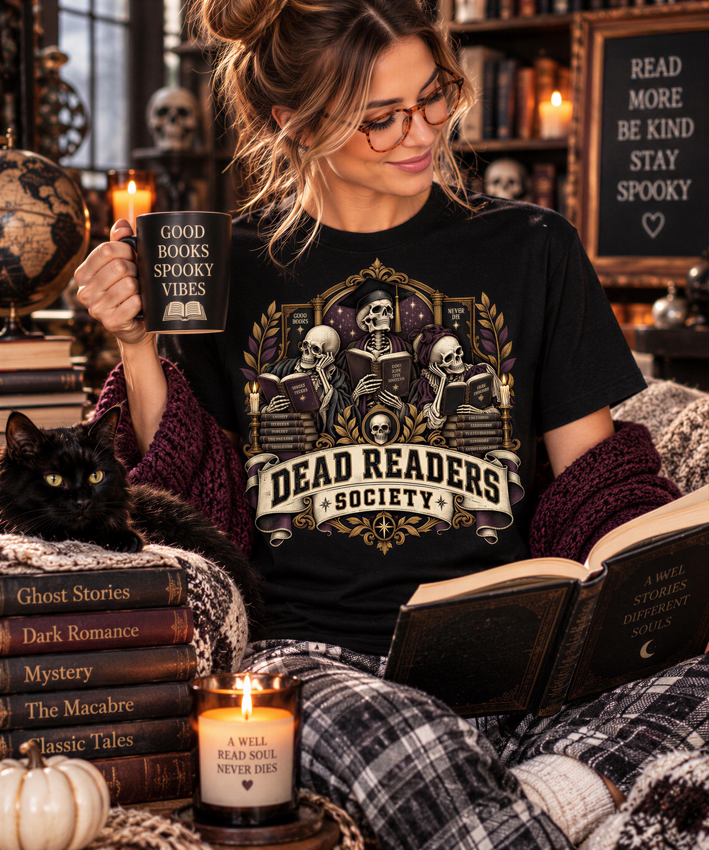 A woman is sitting in a cozy room, reading a book and holding a mug with the text "GOOD BOOK SPOKY VIBES" and "DEAD READERS SOCIETY" printed on it. She is wearing a black t-shirt with a graphic design of skeletons reading books. The room has a bookshelf filled with books, a candle, and a cat.