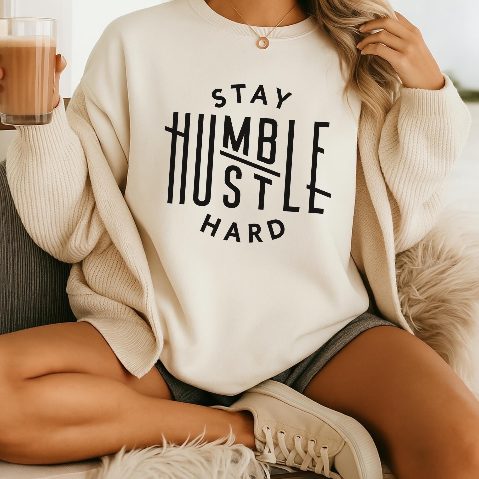 A person sitting on a couch wearing a white sweater with the text "STAY HUMBLE HARD" printed on it.