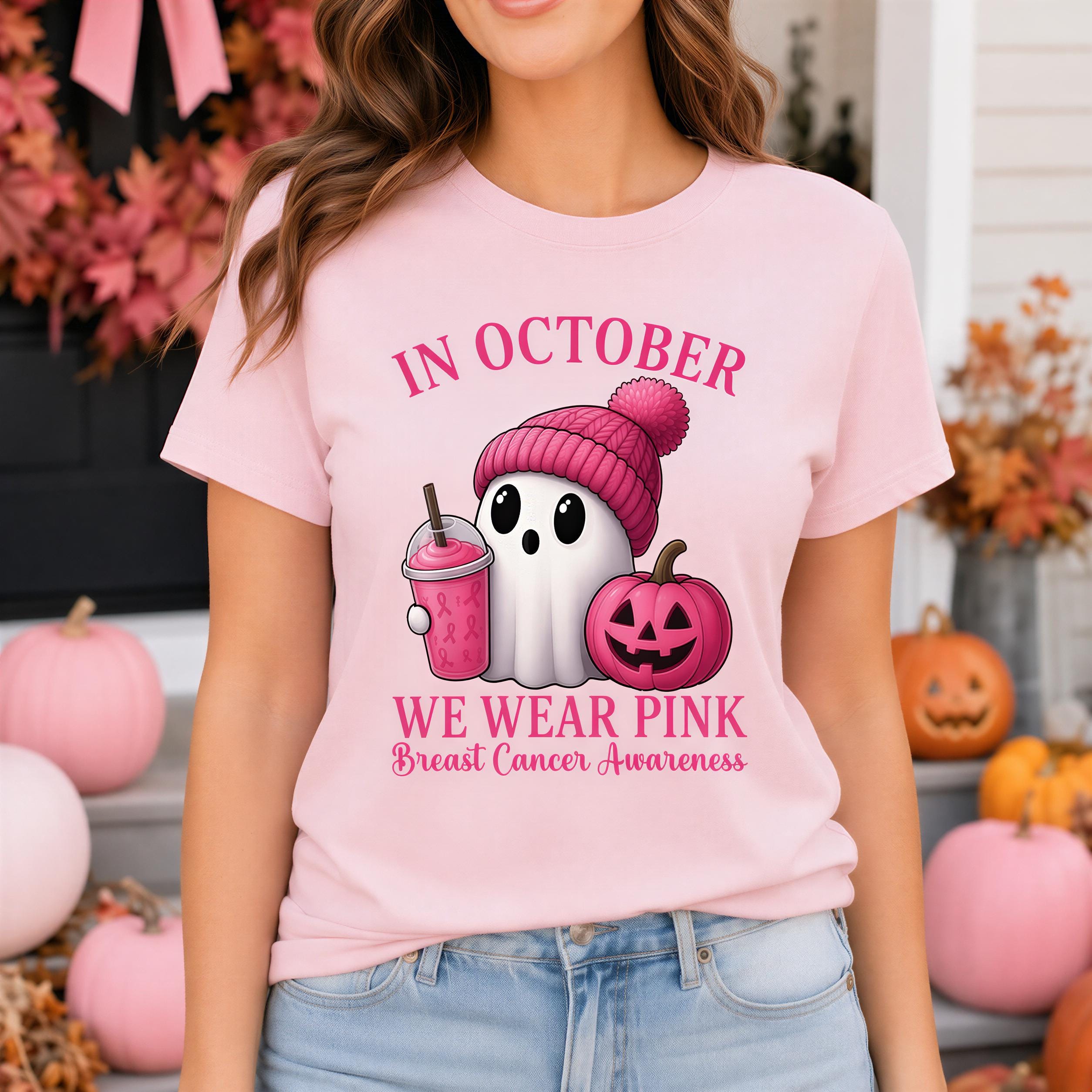 A woman wearing a pink t-shirt with a graphic design of a ghost wearing a pink hat and holding a pumpkin, along with the text "In October WE WEAR PINK Breast Cancer Awareness".