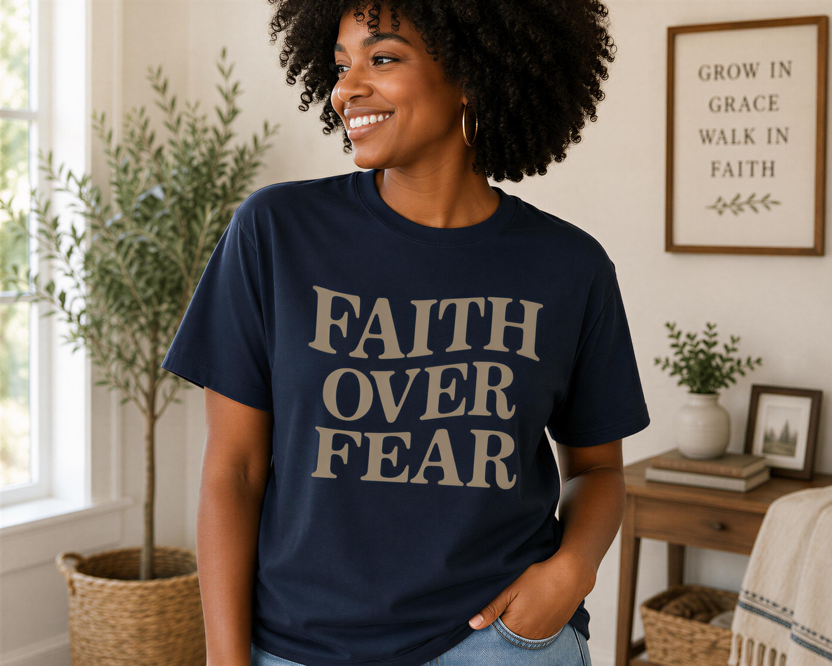 A woman with curly hair is smiling and wearing a navy blue t-shirt with the text "FAITH OVER FEAR" printed on it.