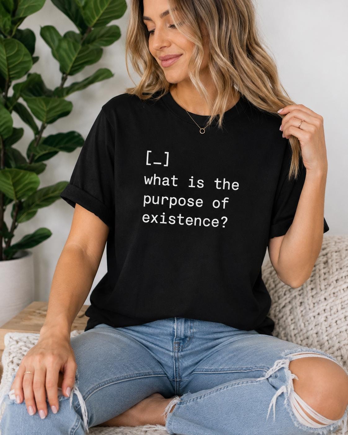 A woman wearing a black t-shirt with the text "What is the purpose of existence?" is sitting on a couch, looking at the camera.