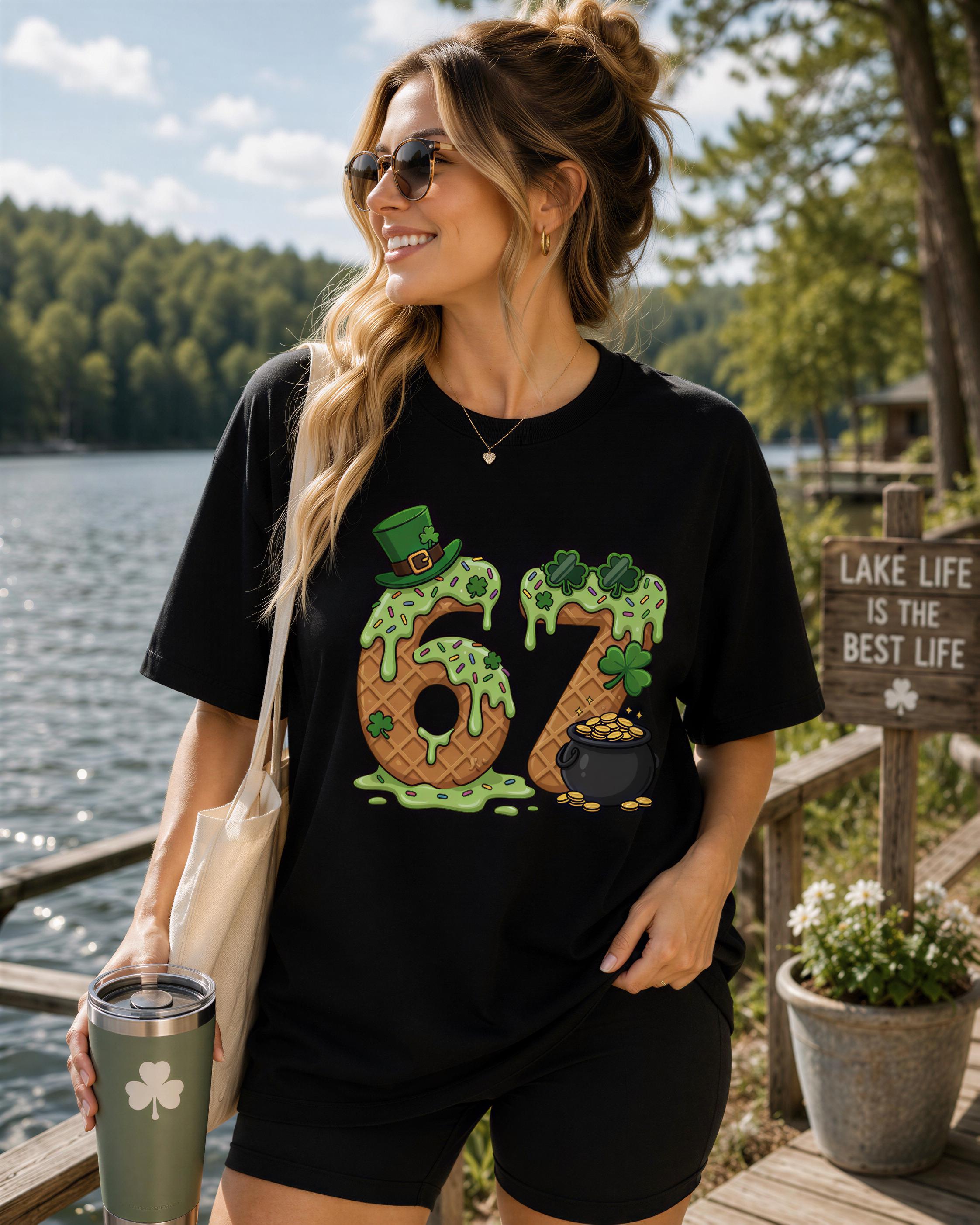 A woman wearing a black t-shirt with a graphic design of the number 6 and a leprechaun, standing near a lake and holding a cup.