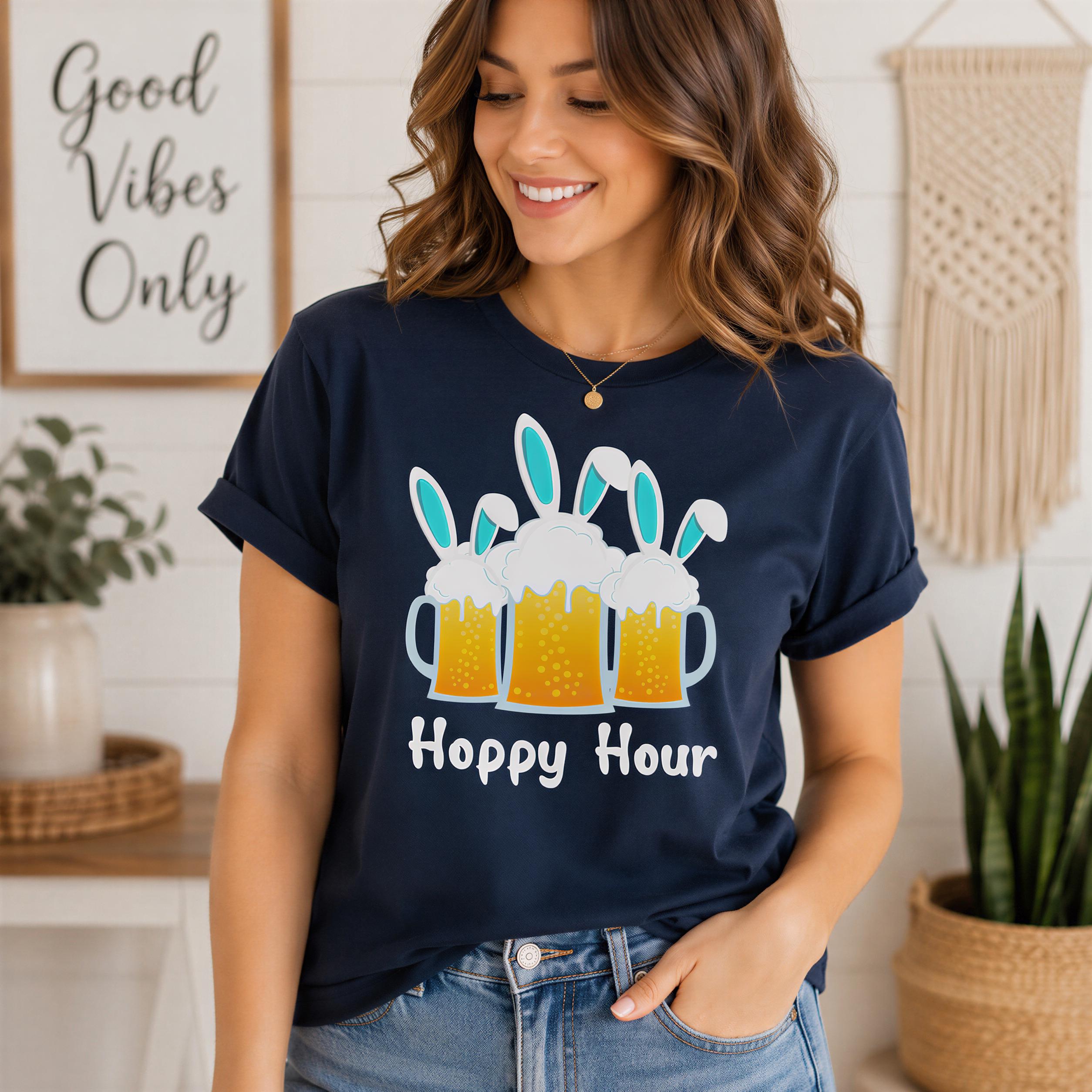 A woman wearing a navy blue t-shirt with a graphic of beer mugs and the text "Hoppy Hour" is smiling and posing in a room with a "Good Vibes Only" sign and potted plants in the background.