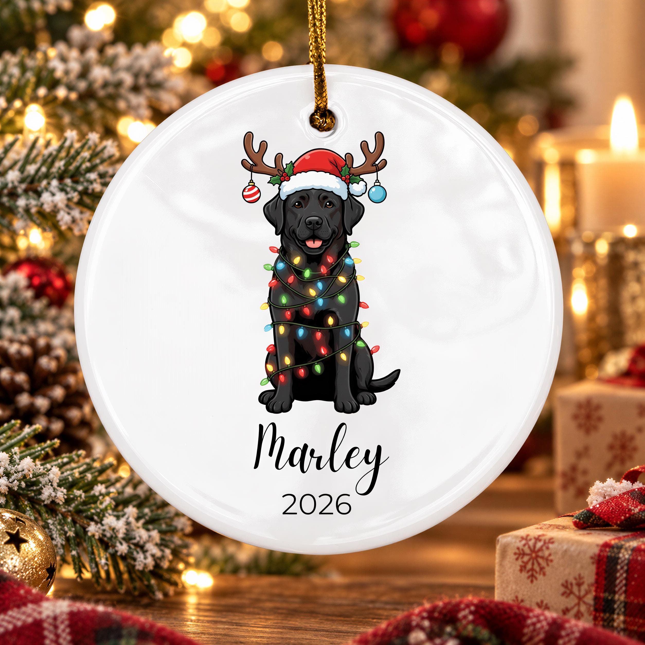 A white ornament with a black dog wearing a Santa hat and Christmas lights around its neck, with the name "Marley" and the year "2026" printed below.