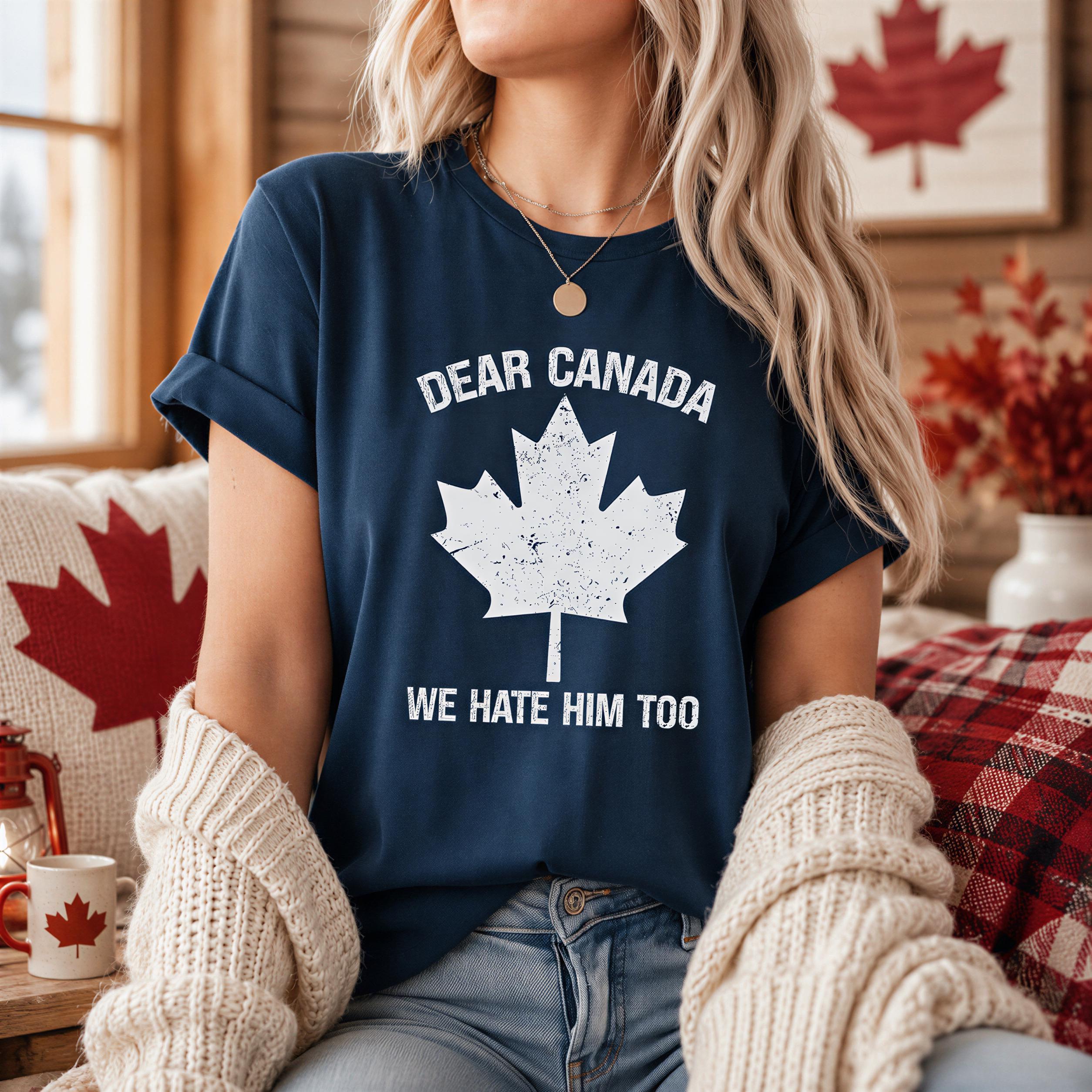A woman wearing a navy blue t-shirt with a white maple leaf graphic and the text "DEAR CANADA WE HATE HIM TOO" is sitting on a couch with a white sweater draped over her shoulders.