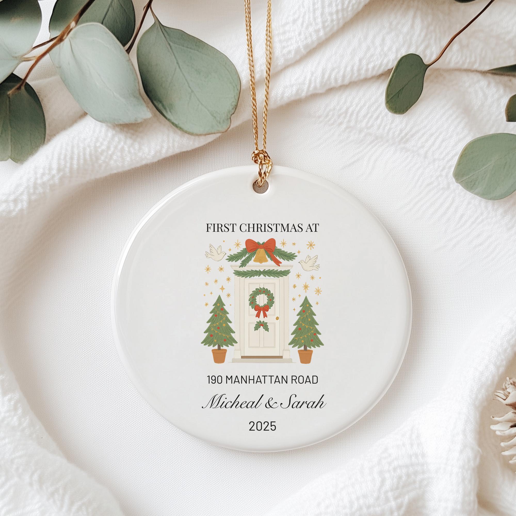 A white ceramic ornament with a Christmas tree and wreath design hangs on a white fabric surface.