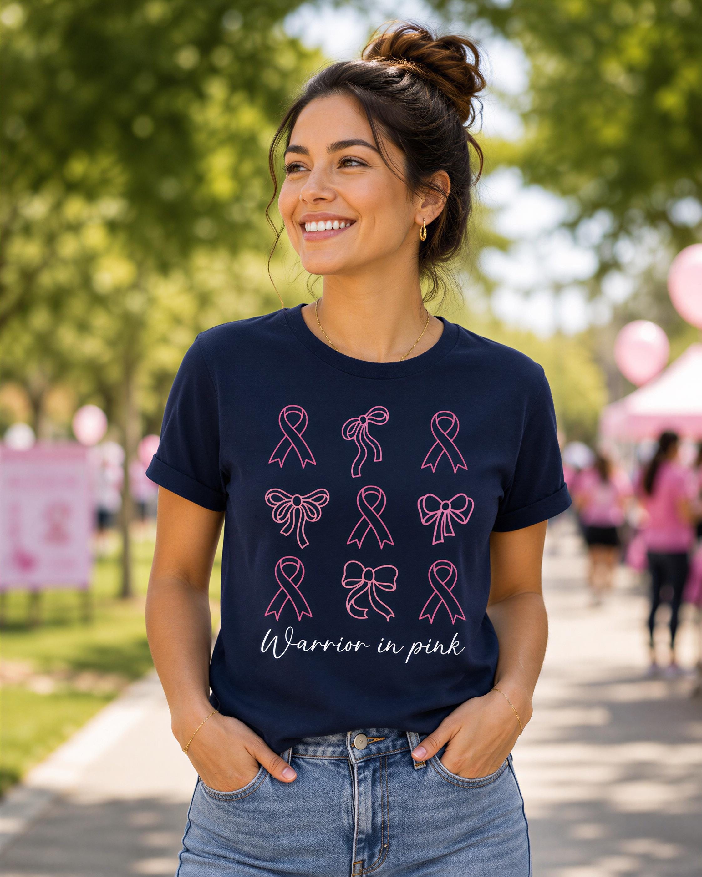 A woman wearing a navy blue t-shirt with pink ribbon designs and the text "Warrior in pink" is smiling and standing outdoors.