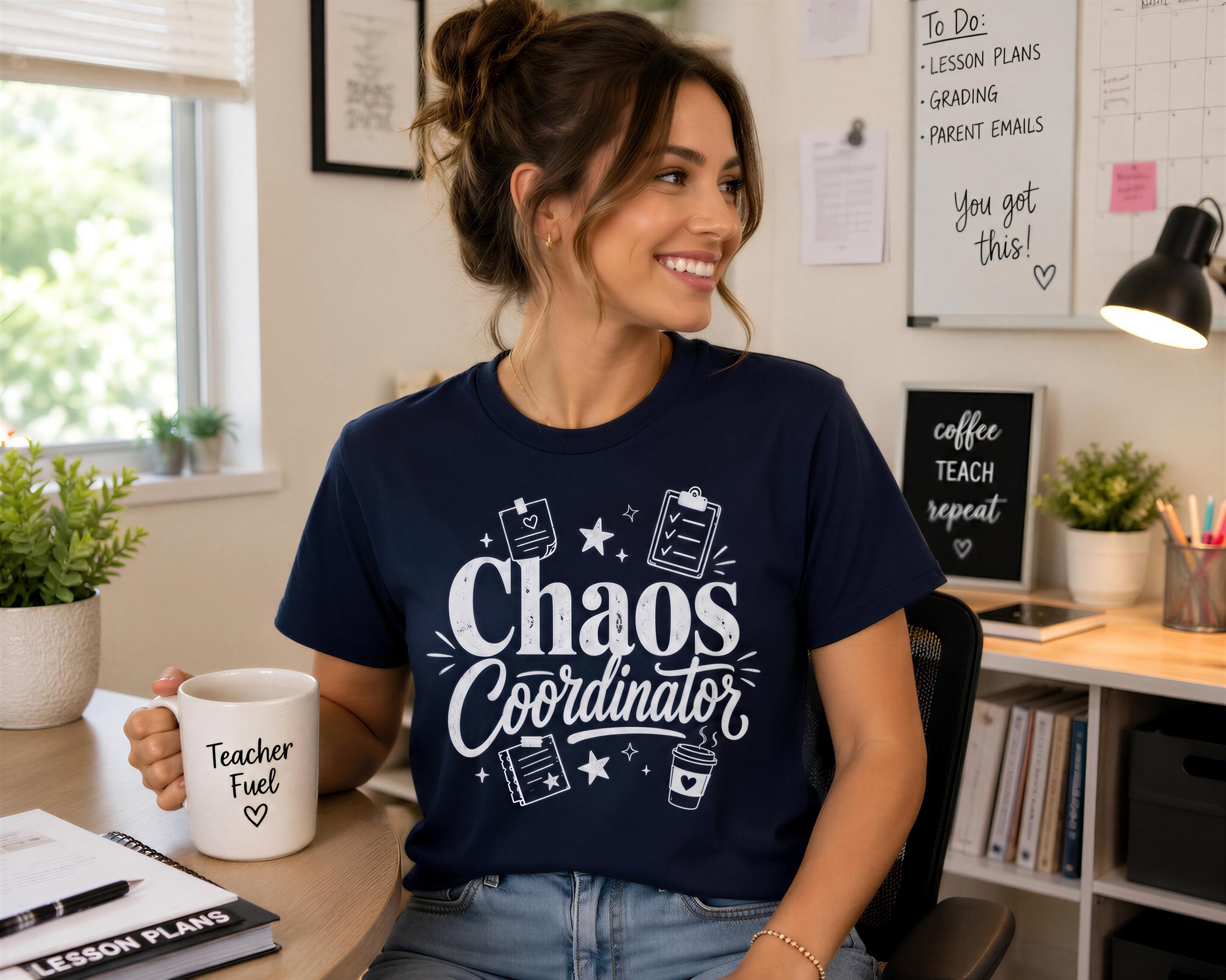 A woman wearing a navy blue t-shirt with the text "Chaos Coordinator" is sitting at a desk in a home office, smiling and looking to the side.