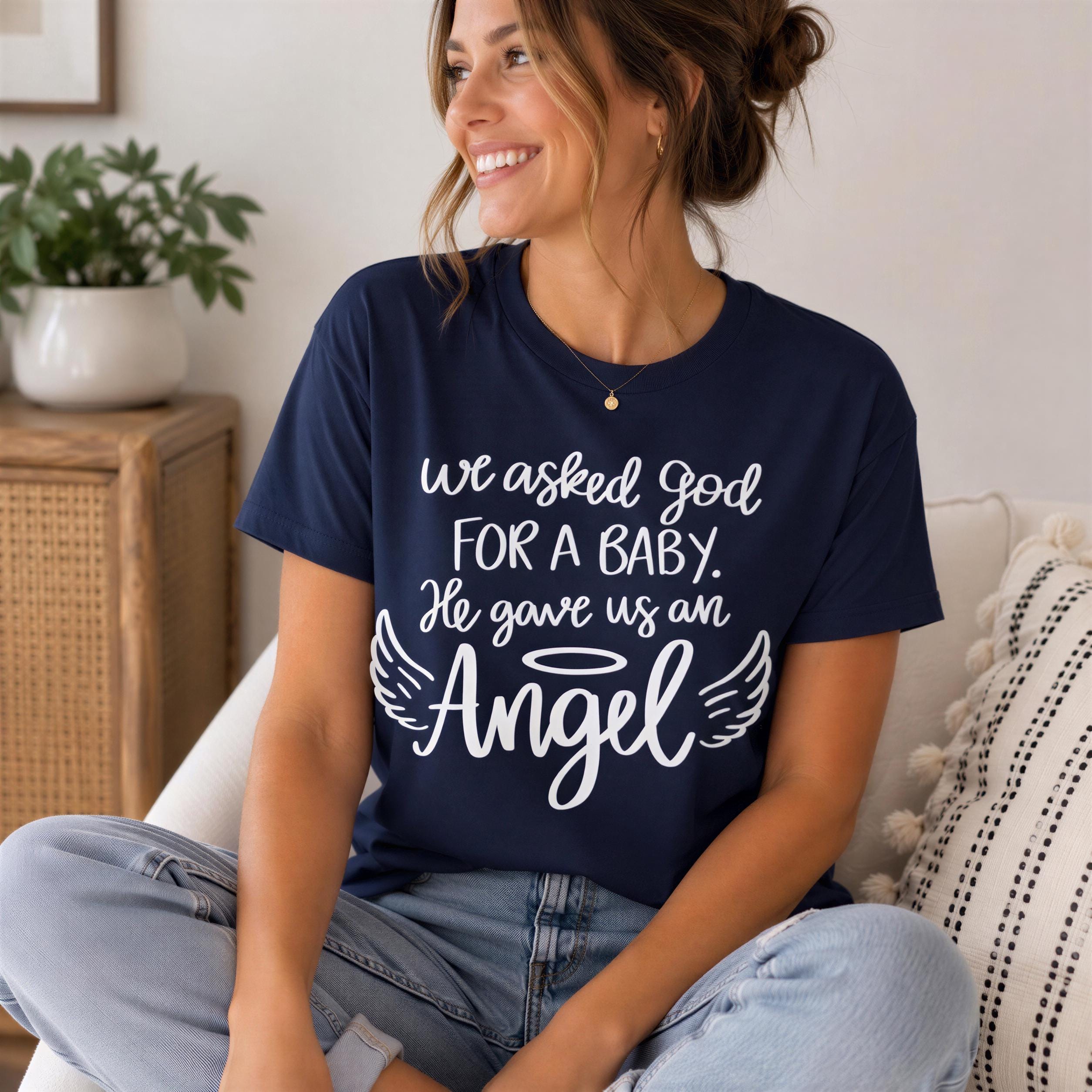 A woman wearing a navy blue t-shirt with white text and a graphic design, sitting on a couch and smiling.