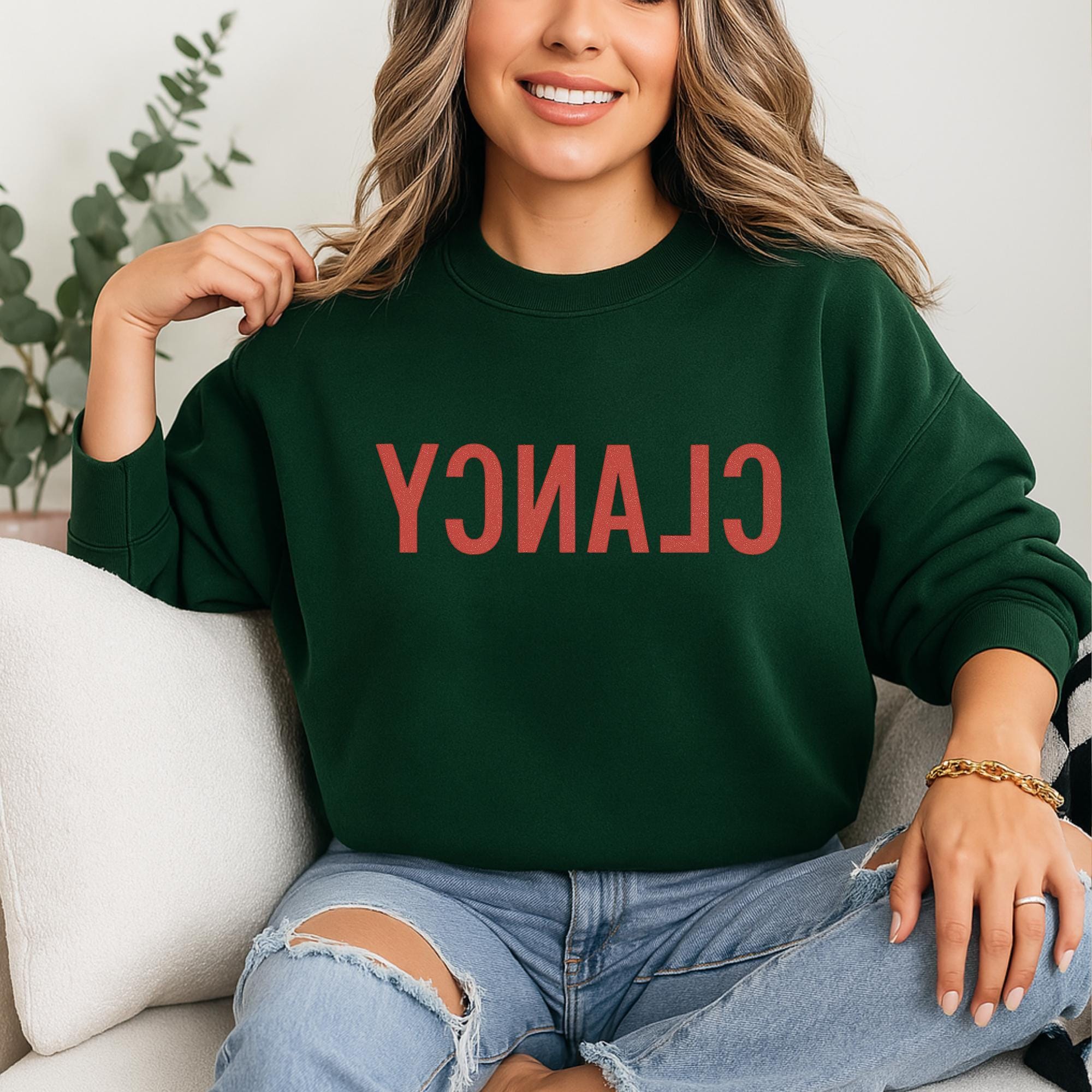 A woman wearing a green sweatshirt with the word "CLAN" printed on it, sitting on a couch.