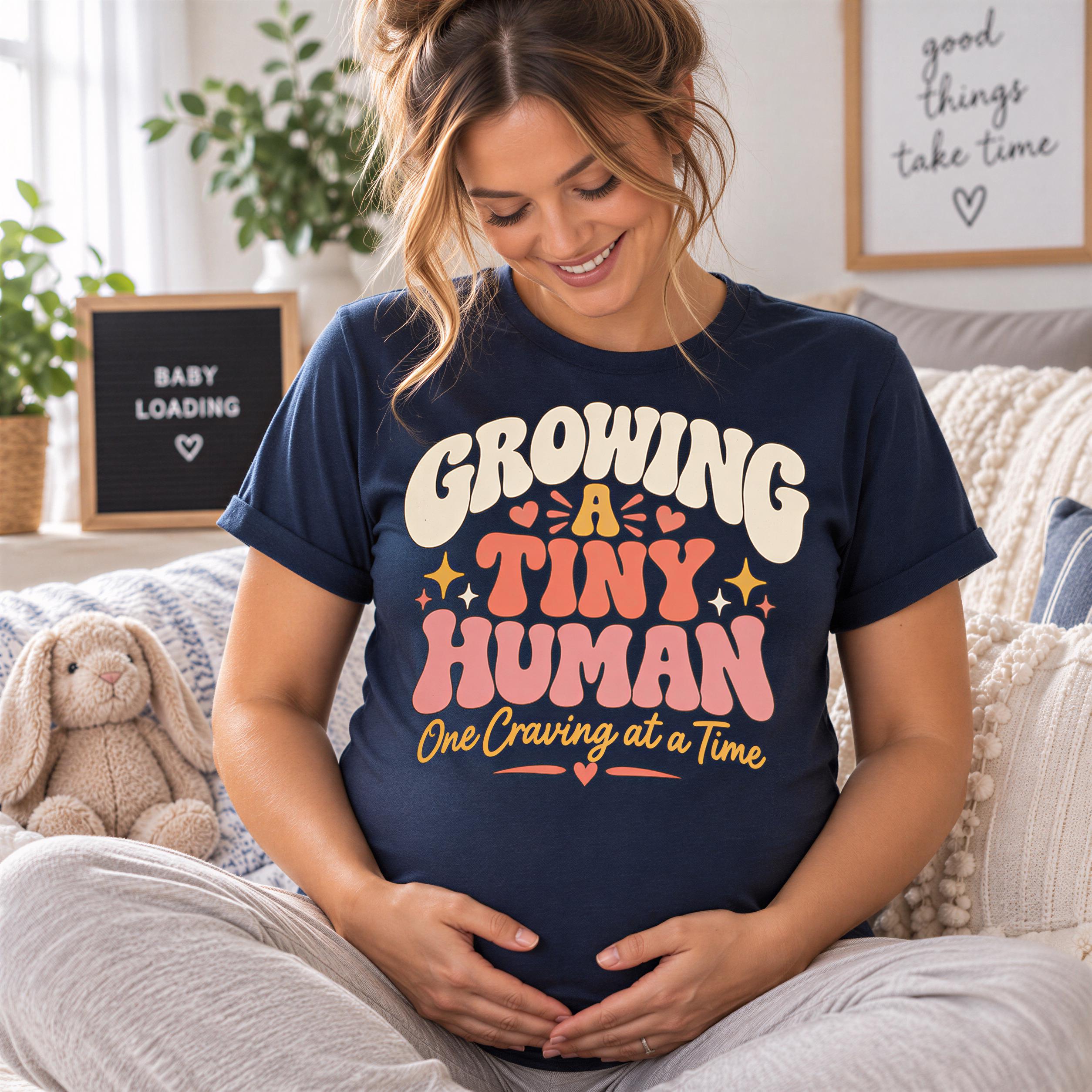A pregnant woman wearing a blue t-shirt with a humorous text, smiling and sitting on a couch.