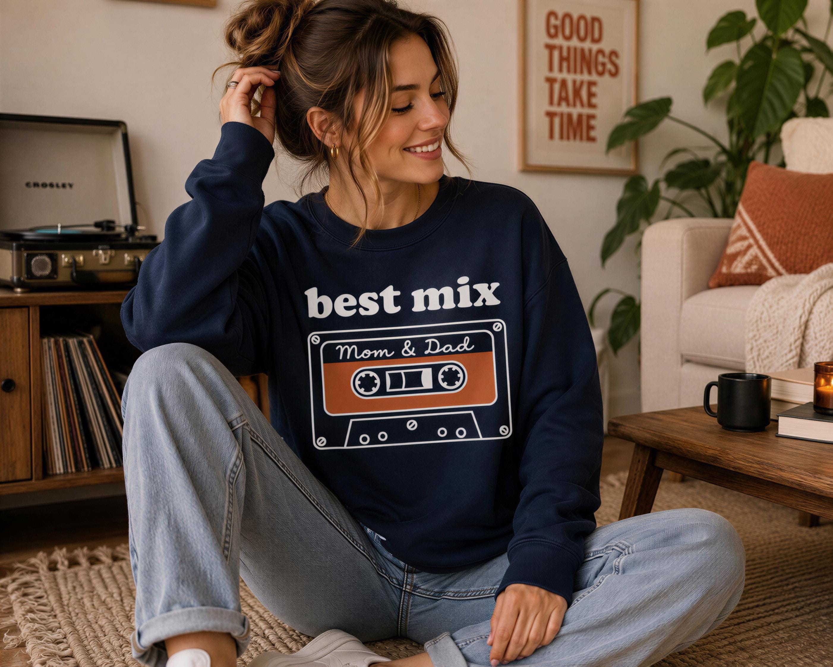 A woman sitting on the floor wearing a navy blue sweatshirt with a graphic design on it.