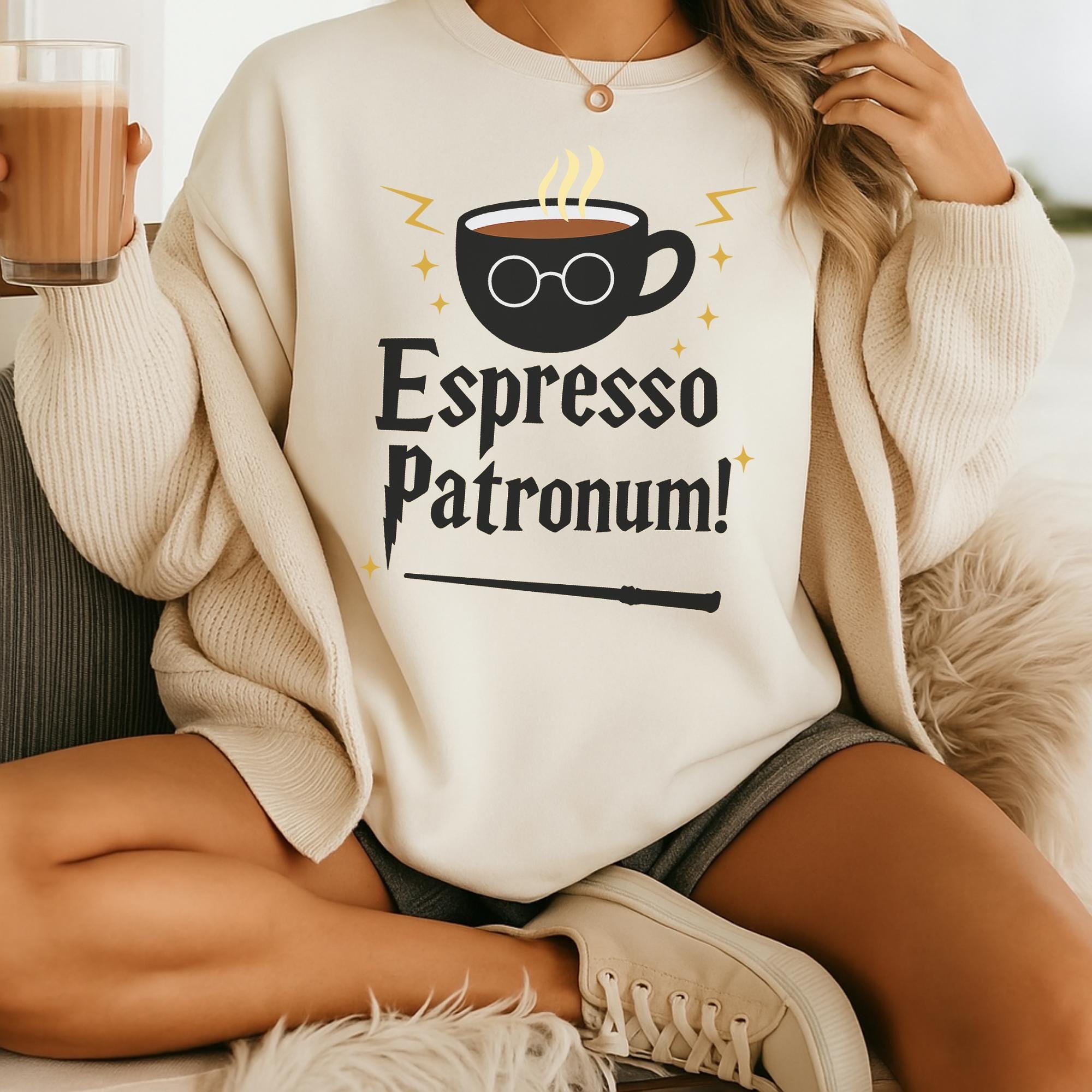 A person wearing a white sweater with a graphic design on it, holding a drink in their hand.