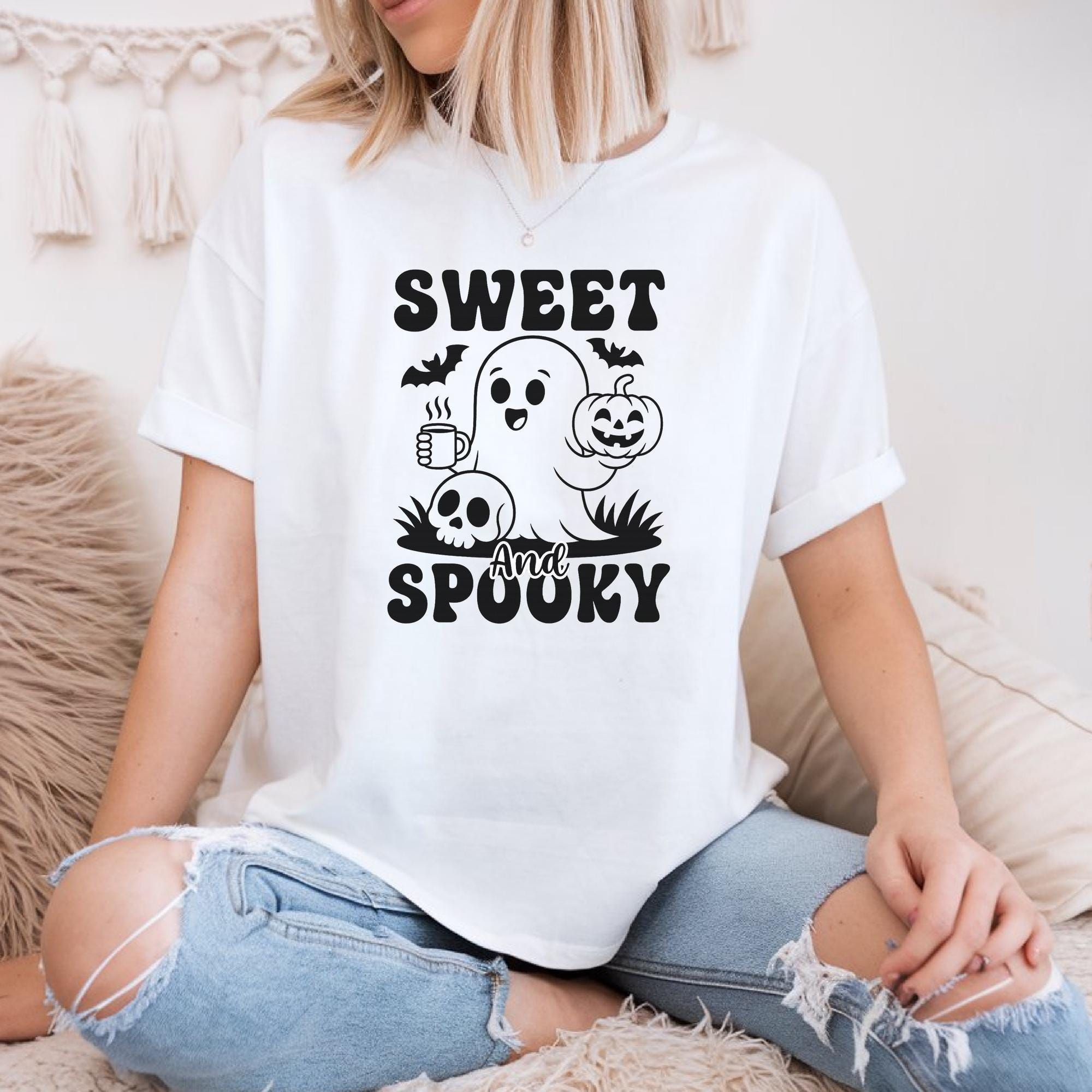 A woman wearing a white t-shirt with a graphic design featuring a ghost, pumpkin, and the text "Sweet and Spooky".