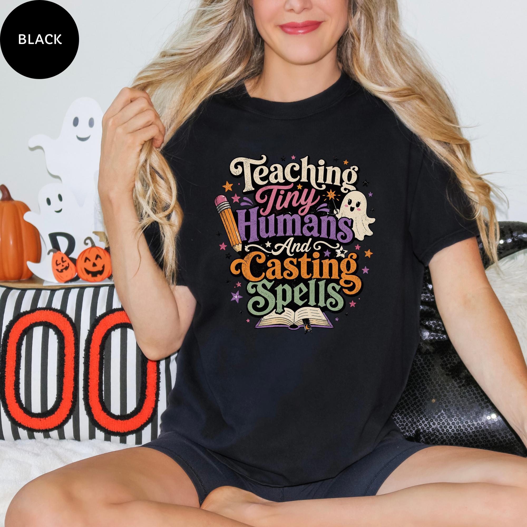 A woman wearing a black t-shirt with a Halloween-themed design, sitting on a couch with Halloween decorations in the background.