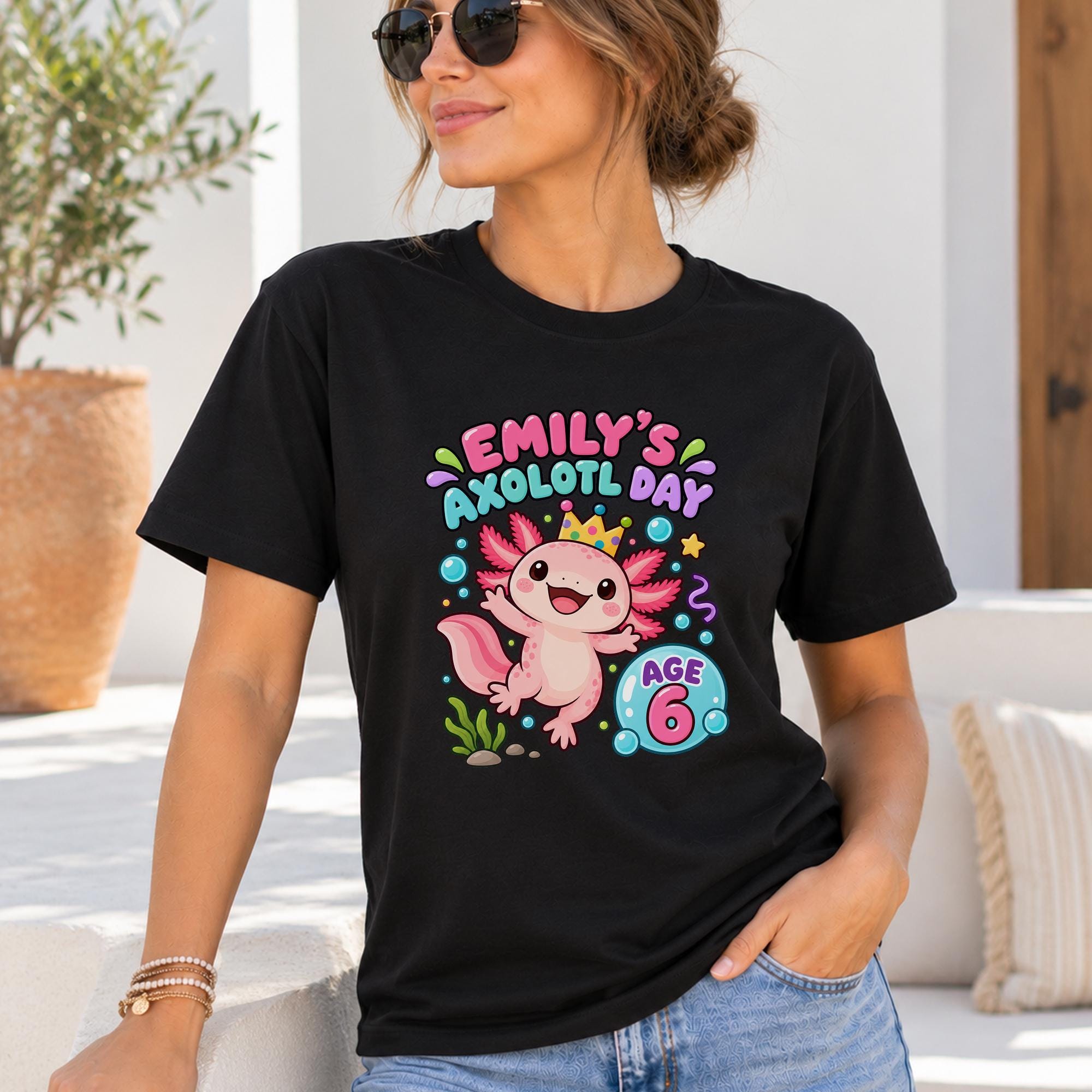 A woman wearing a black t-shirt with a graphic of an axolotl, a type of salamander, and text that says "Emily's axolotl day age 6".