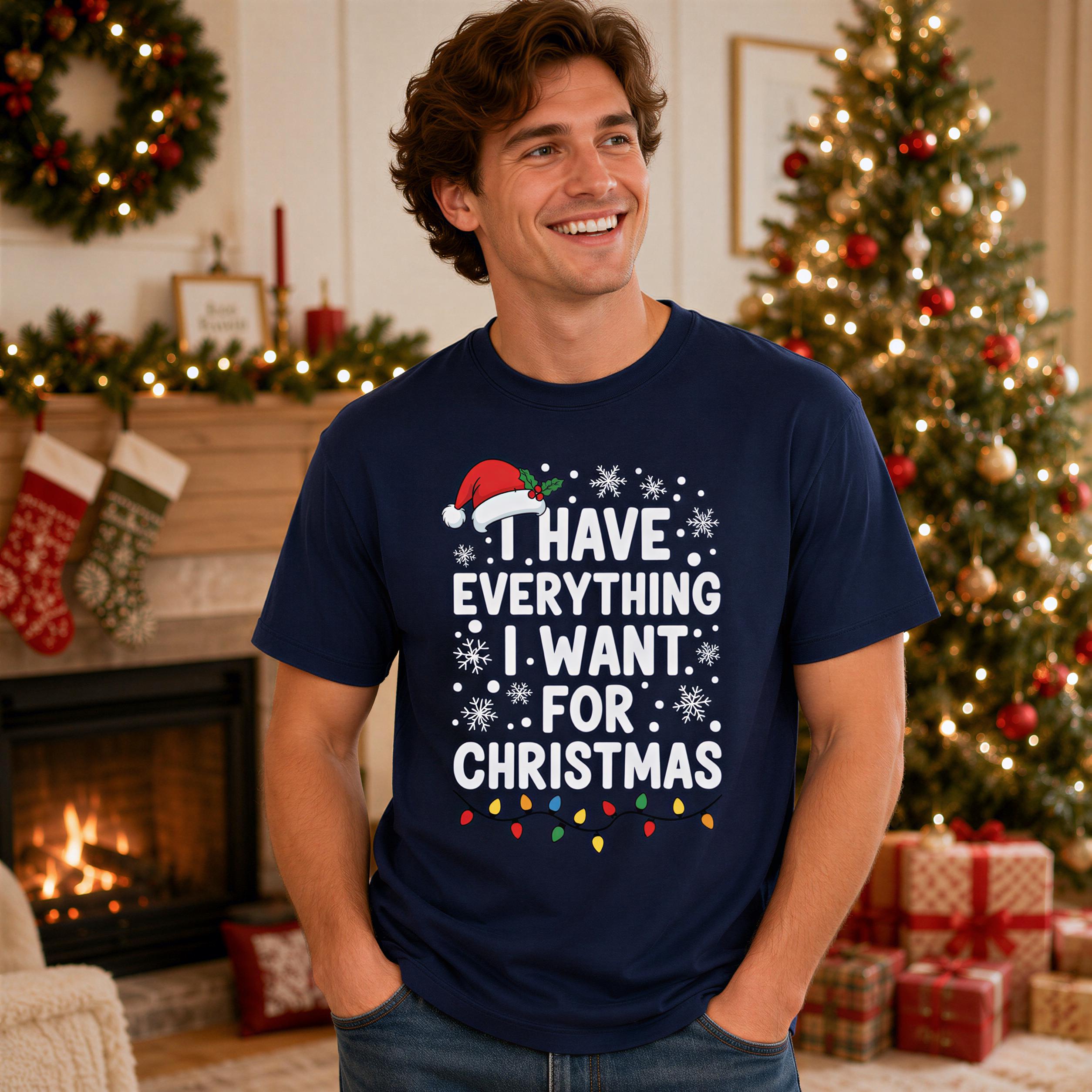 A man wearing a navy blue t-shirt with a humorous Christmas-themed text stands in front of a decorated Christmas tree.