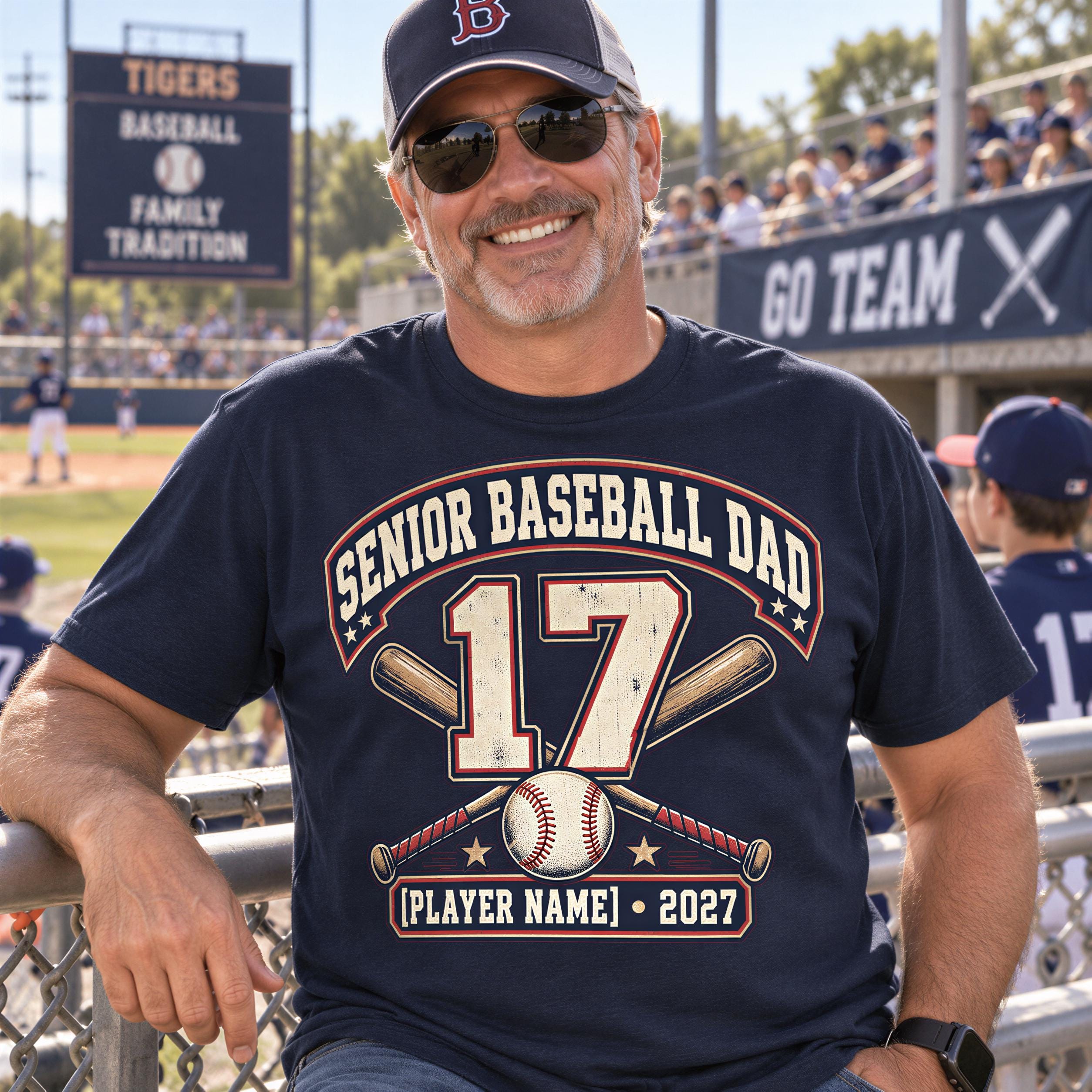 A man wearing a baseball cap and sunglasses is sitting in a stadium, smiling and wearing a t-shirt with a baseball design and the number 17.