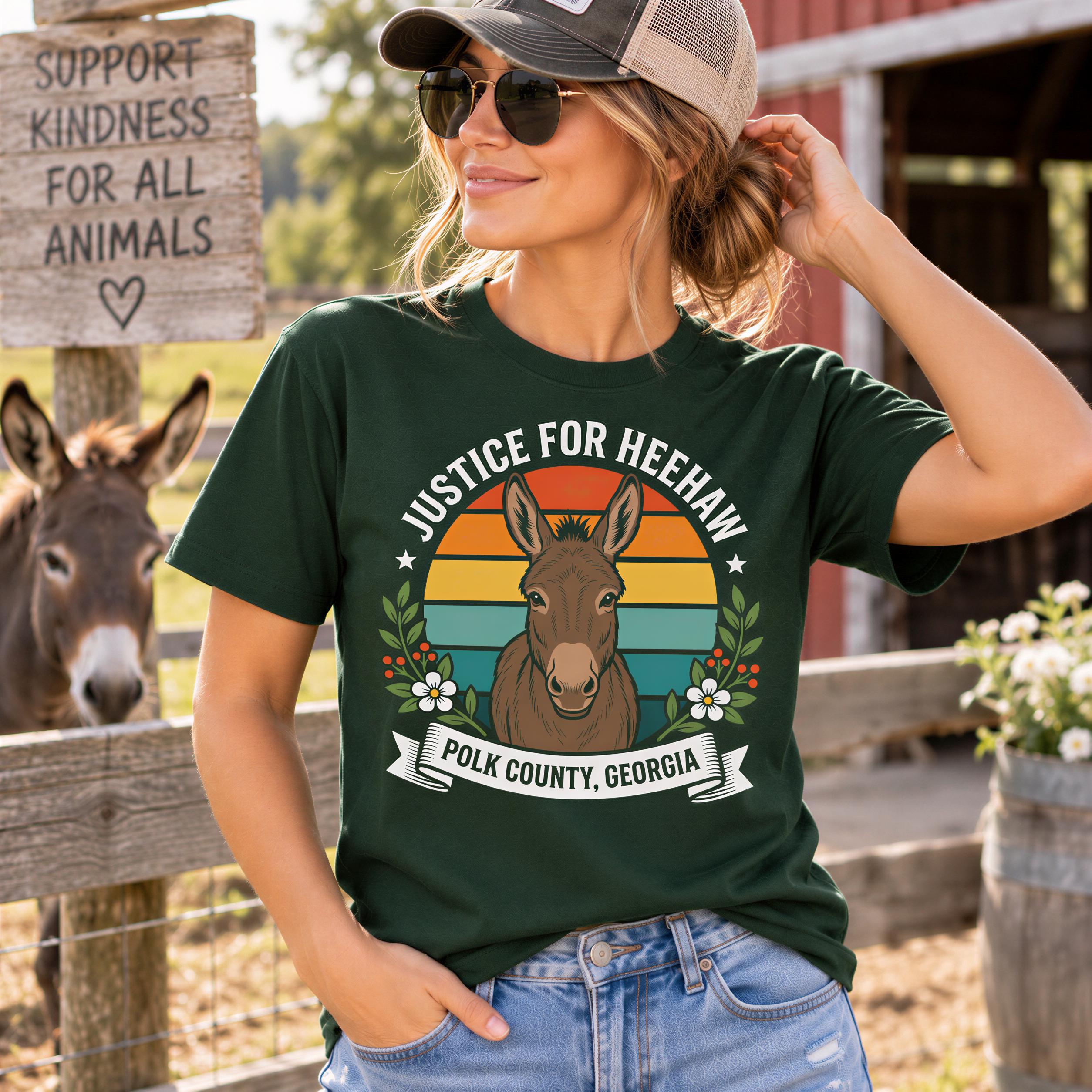 A woman wearing a green t-shirt with a graphic of a donkey and the text "Justice for heehaw" stands in front of a wooden fence, with a donkey visible in the background.