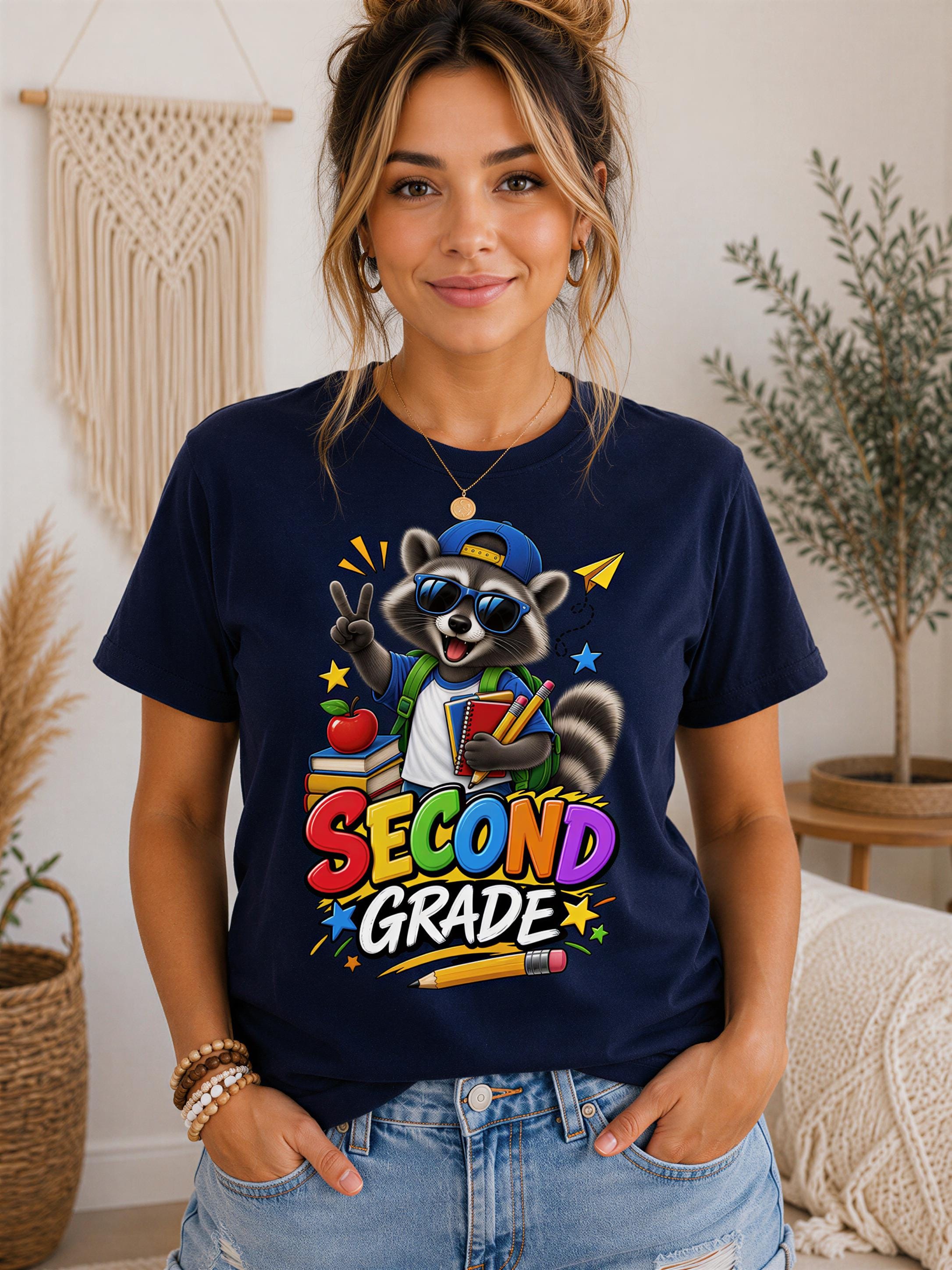 A woman wearing a navy blue t-shirt with a graphic of a raccoon holding a "Second Grade" sign, surrounded by colorful stars and a pencil.