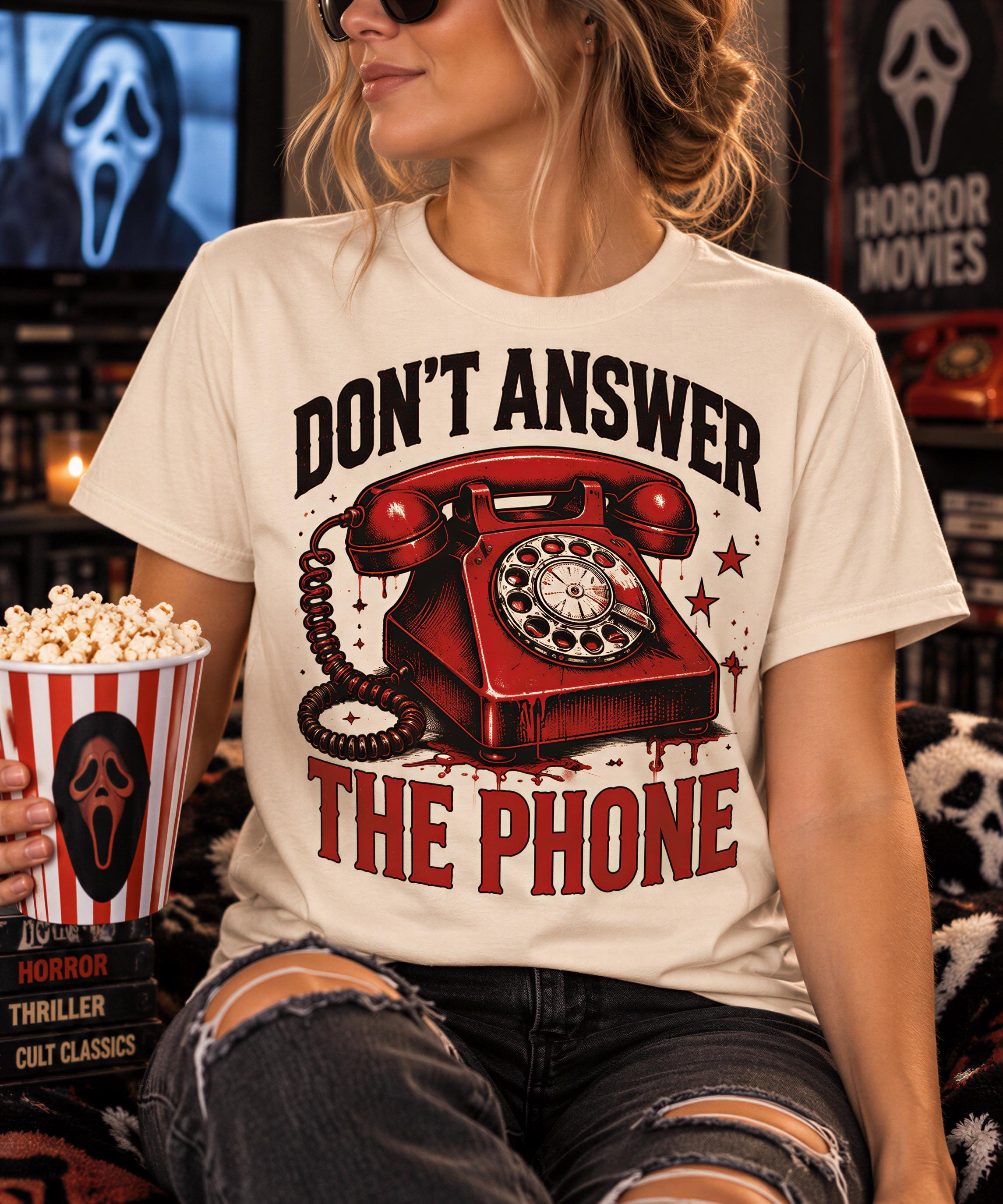 A woman wearing a white t-shirt with a graphic design of a red telephone and the text "DON'T ANSWER THE PHONE" is sitting on a couch while holding a bucket of popcorn and watching a movie.
