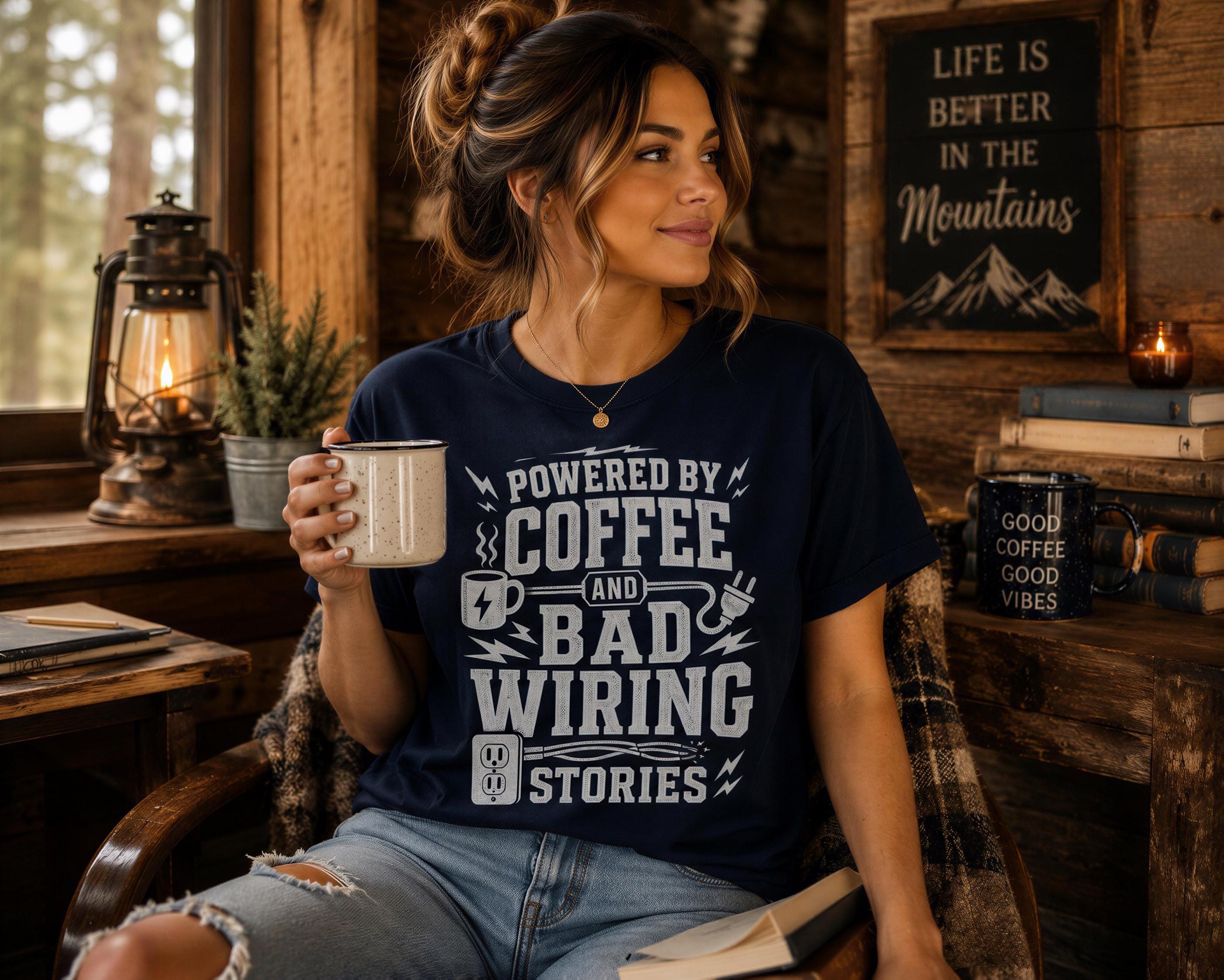 A woman wearing a blue t-shirt with a humorous text printed on it, sitting in a rustic cabin-like setting with a lantern, books, and a mug of coffee.