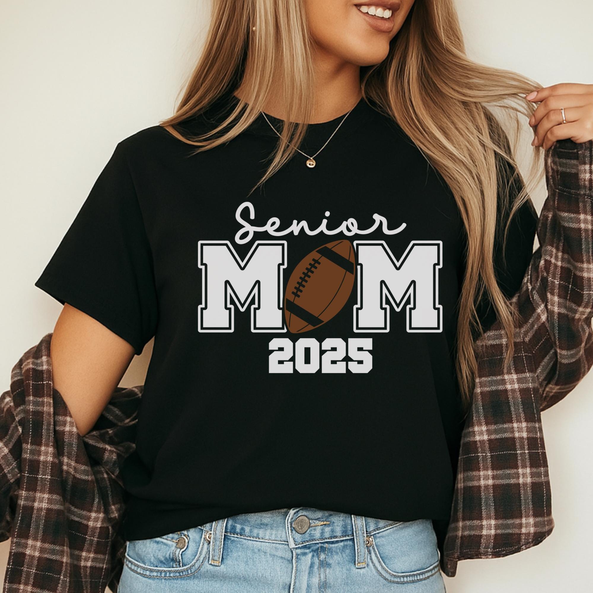 A woman wearing a black t-shirt with the text "Senior Mom 2025" printed on it, smiling and posing with her hair in her hand.