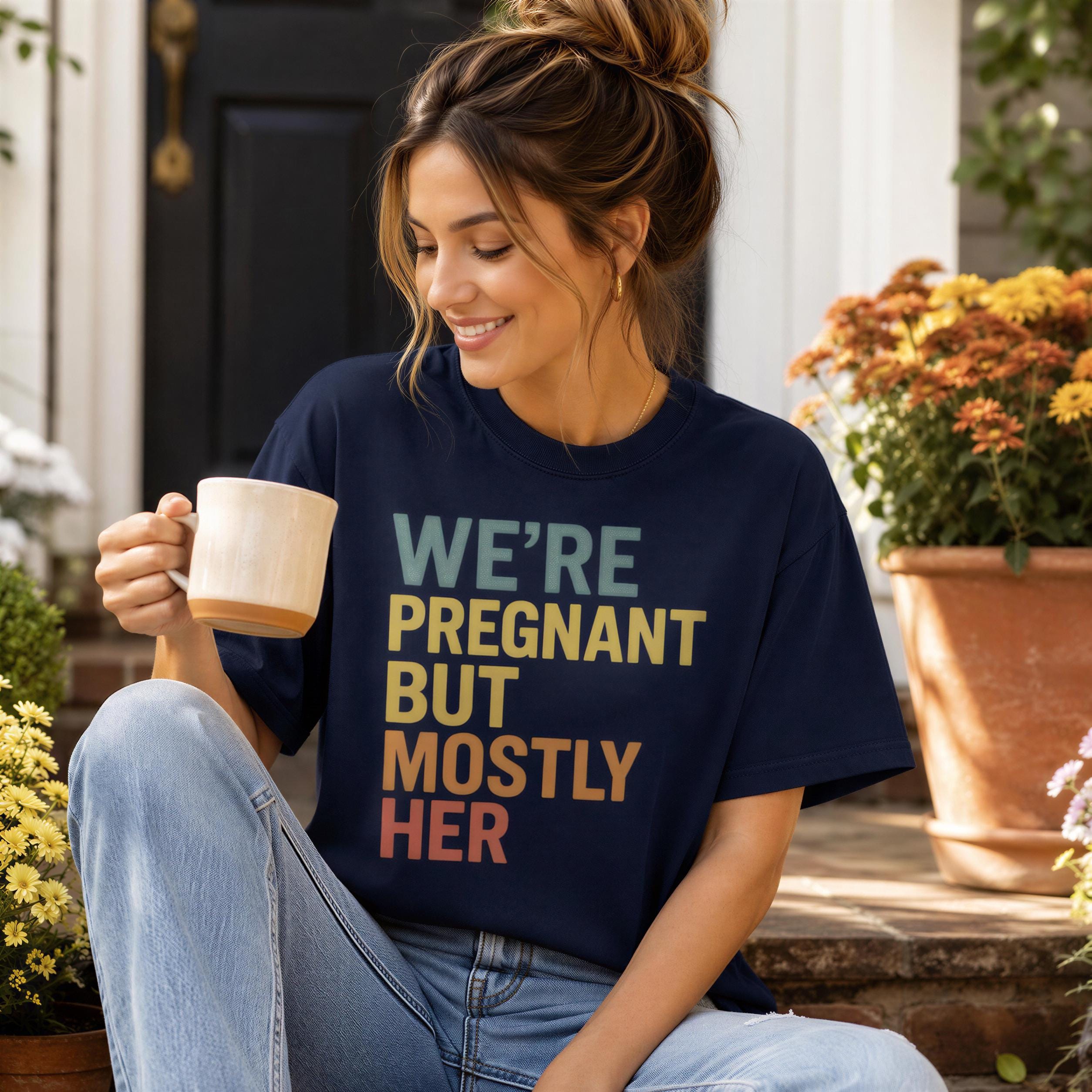 A woman wearing a blue t-shirt with text on it is sitting on a step and holding a coffee mug.