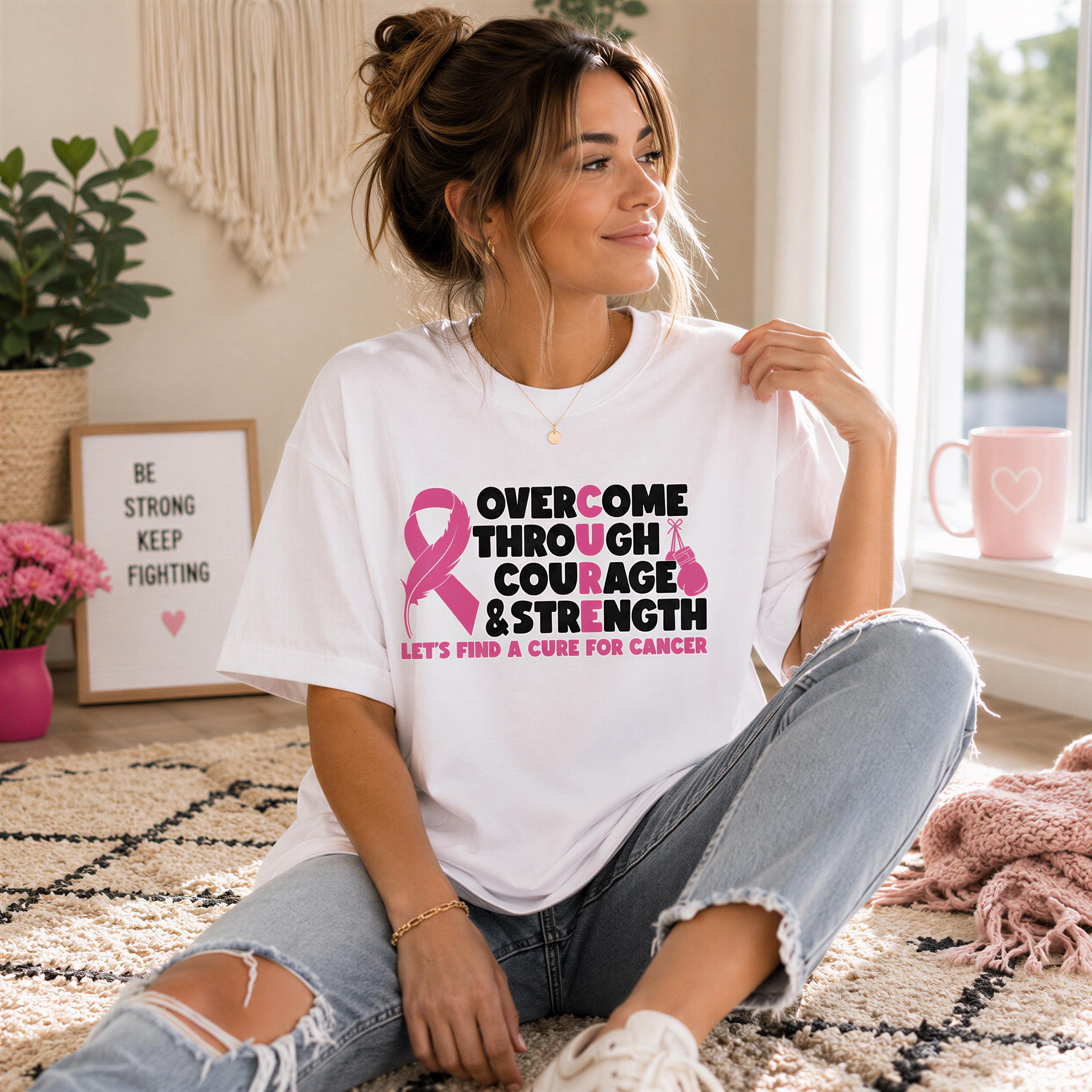 A woman sitting on the floor wearing a white t-shirt with a pink ribbon design and text printed on it.