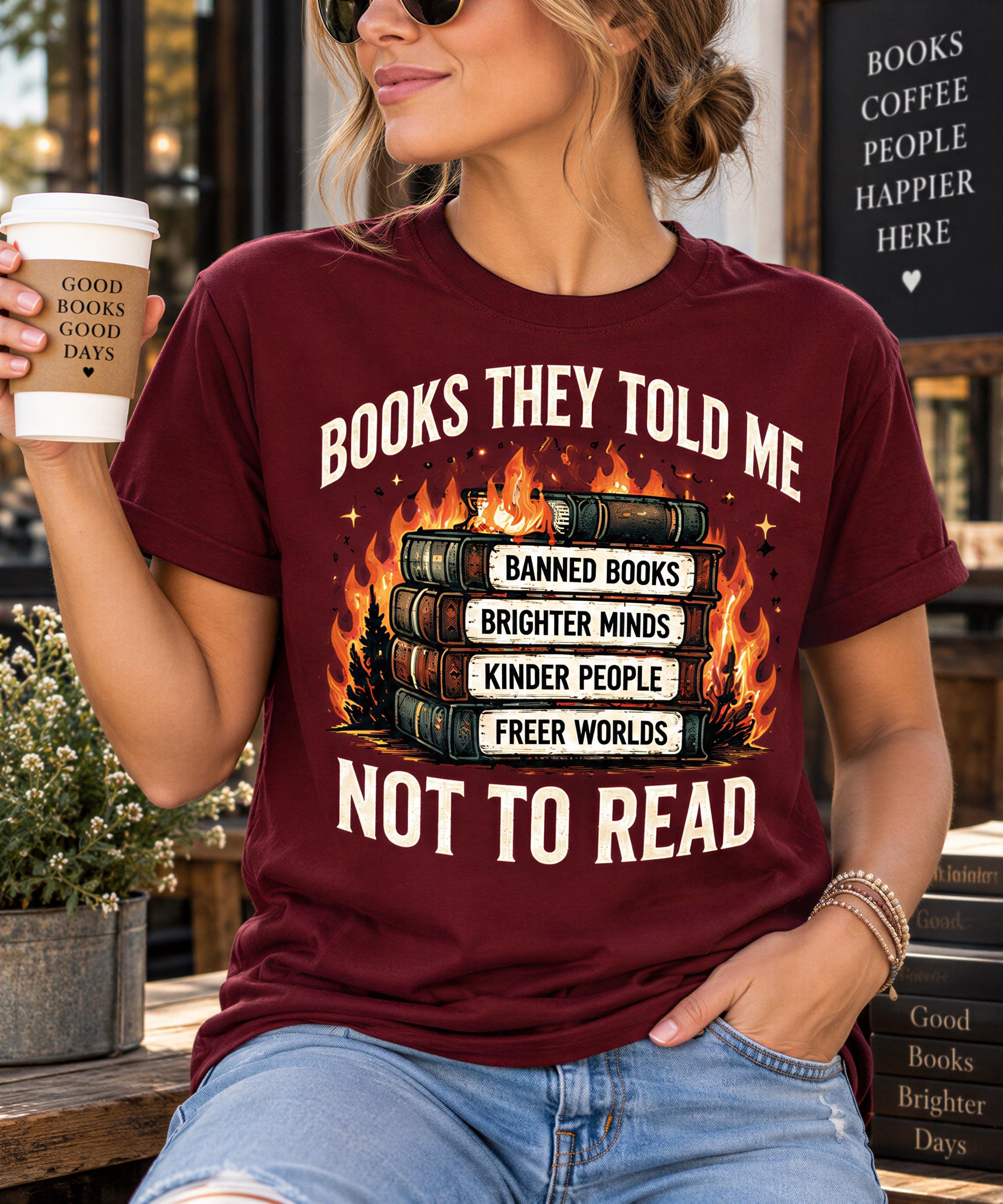 A woman wearing a burgundy t-shirt with a graphic design of books and flames, holding a coffee cup and standing in front of a sign that says "Books coffee people happier here".