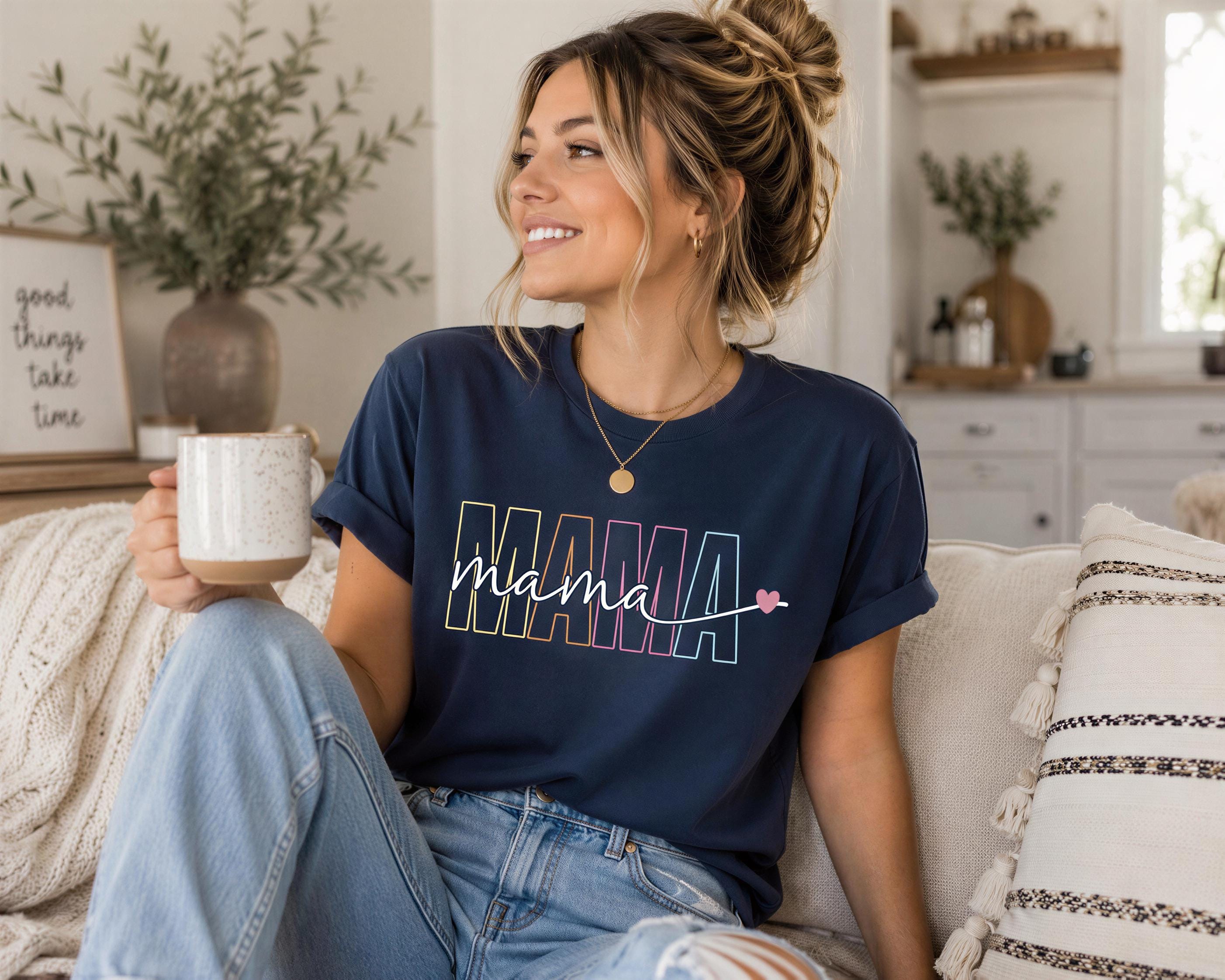 A woman sitting on a couch, holding a coffee mug and wearing a blue t-shirt with the word "Mama" printed on it.