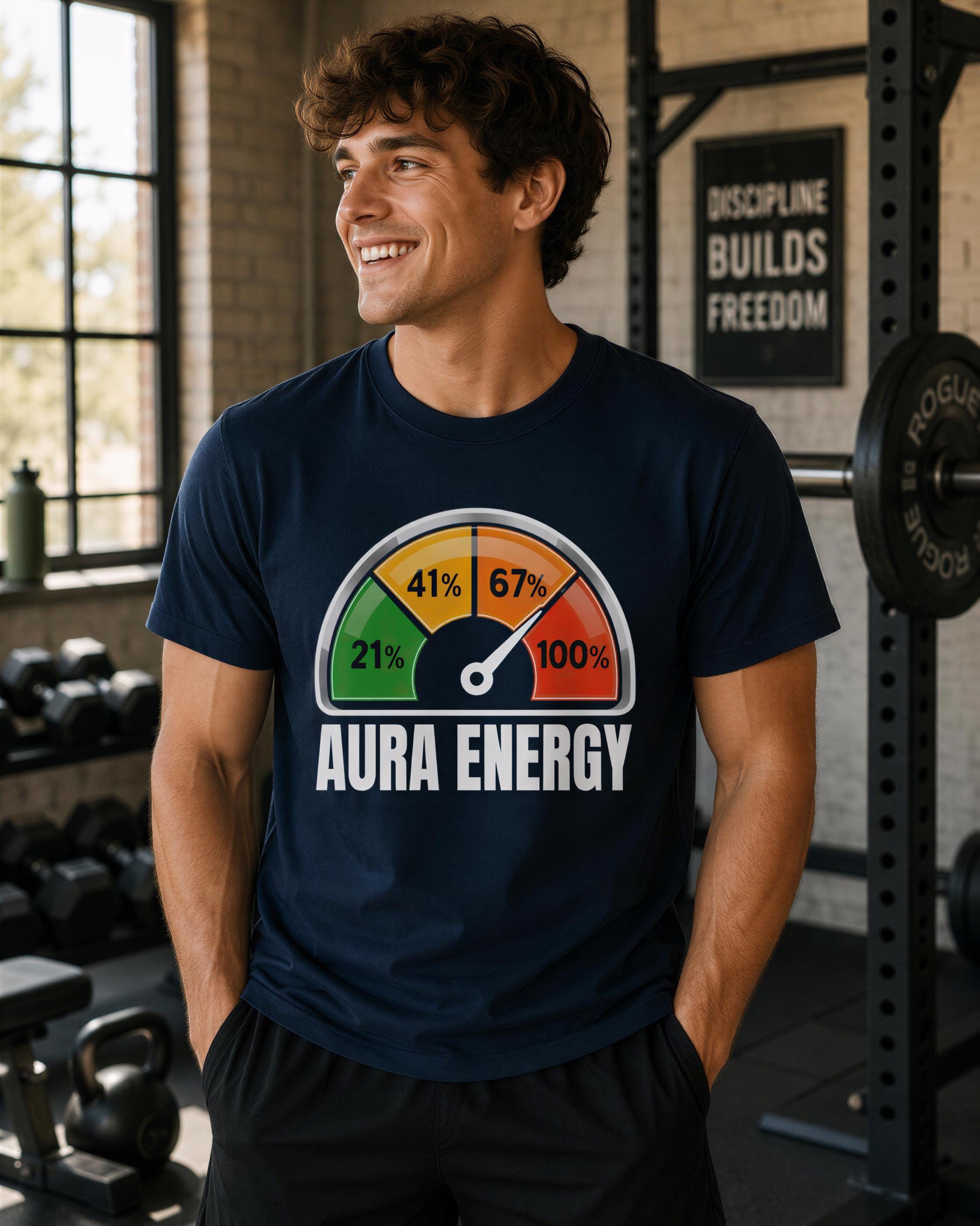A man wearing a navy blue t-shirt with a graphic of a colorful bar graph and the text "AURA ENERGY" is smiling in a gym setting.