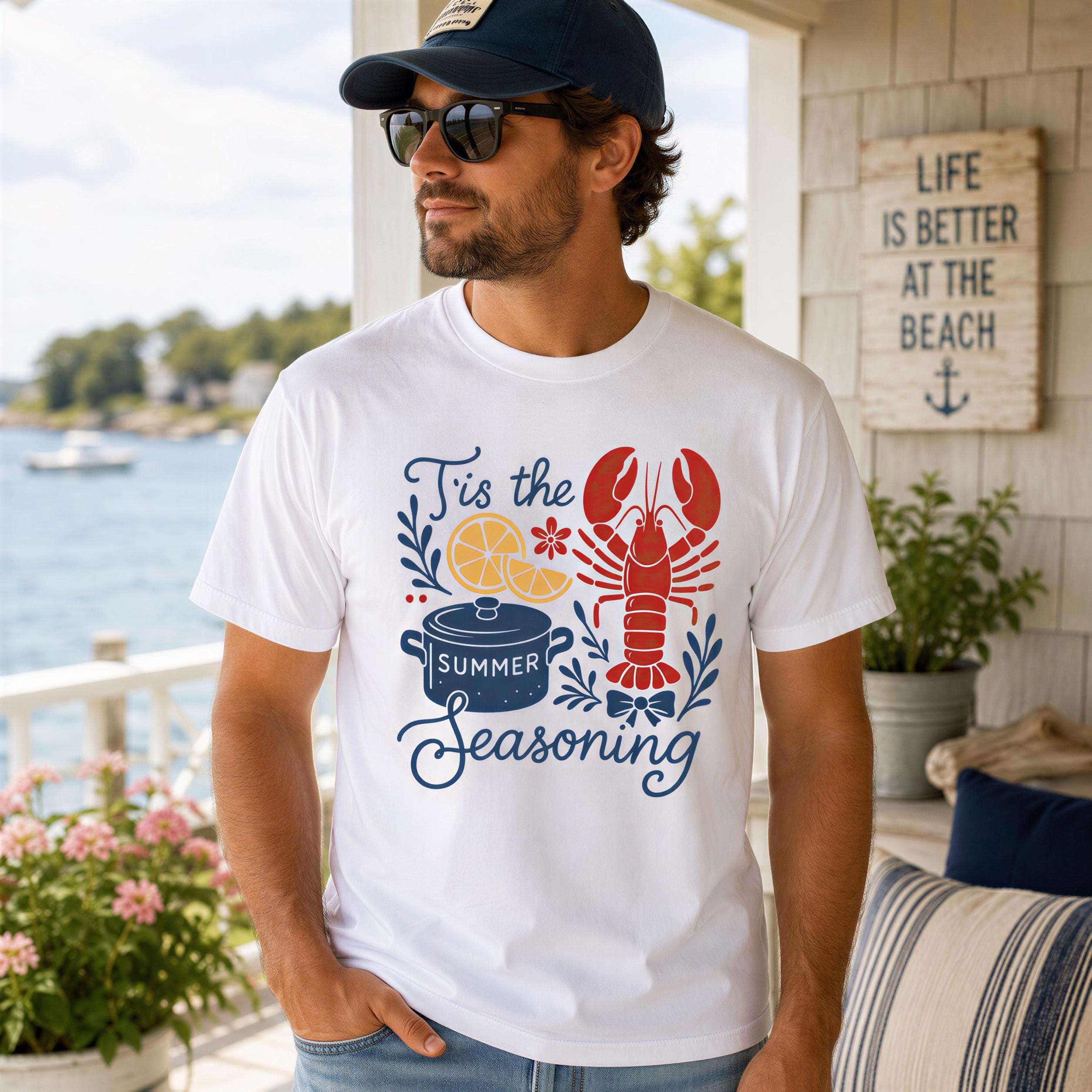 A man wearing a white t-shirt with a lobster graphic and text, standing on a porch with a view of a body of water and a sign that says "Life is better at the beach".